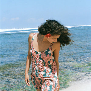 woman with brown hair wearing a blue thin strap tie back romper with red ginger and tiare print.