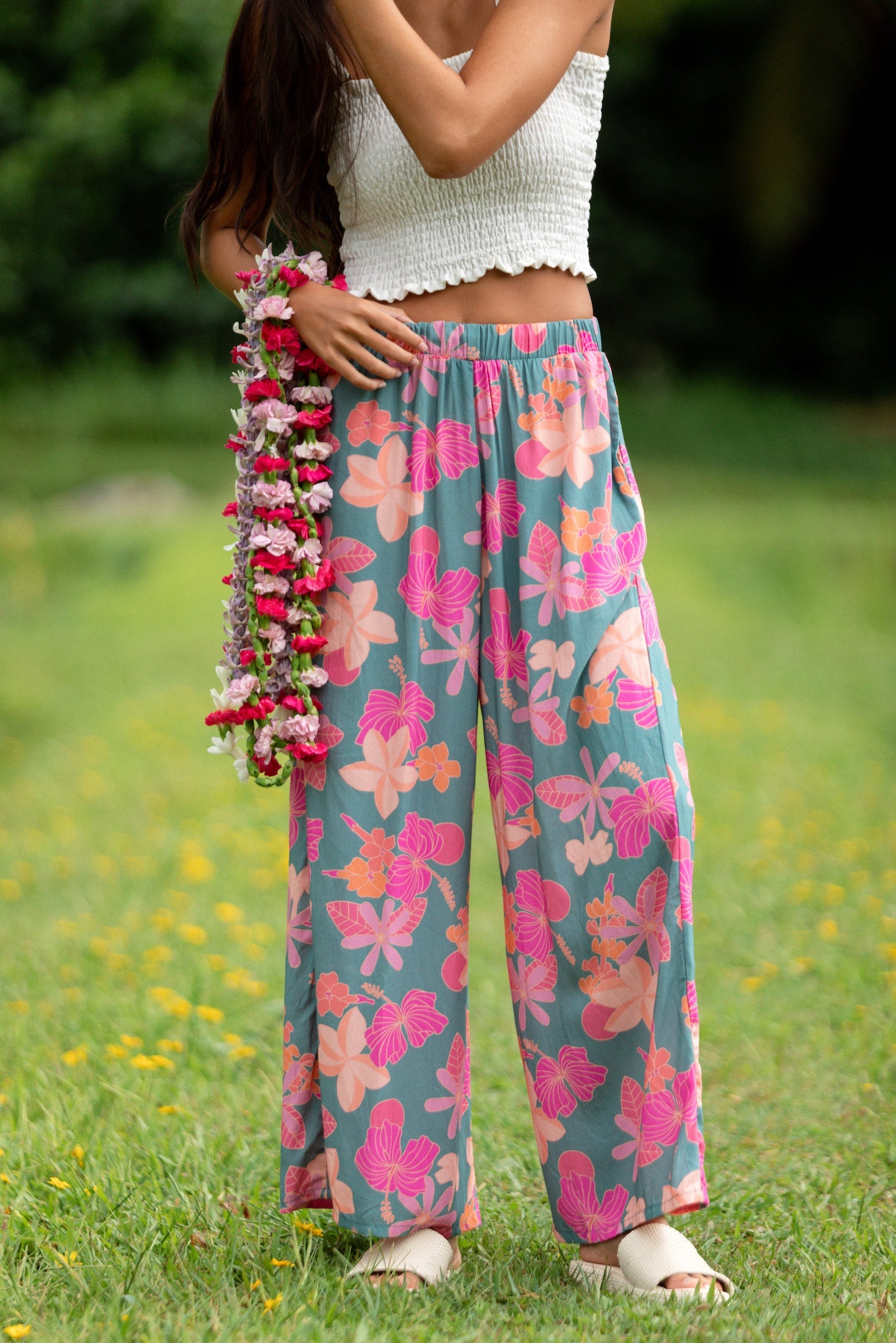woman with brown hair wearing teal flowy pants with orange and pink foral print