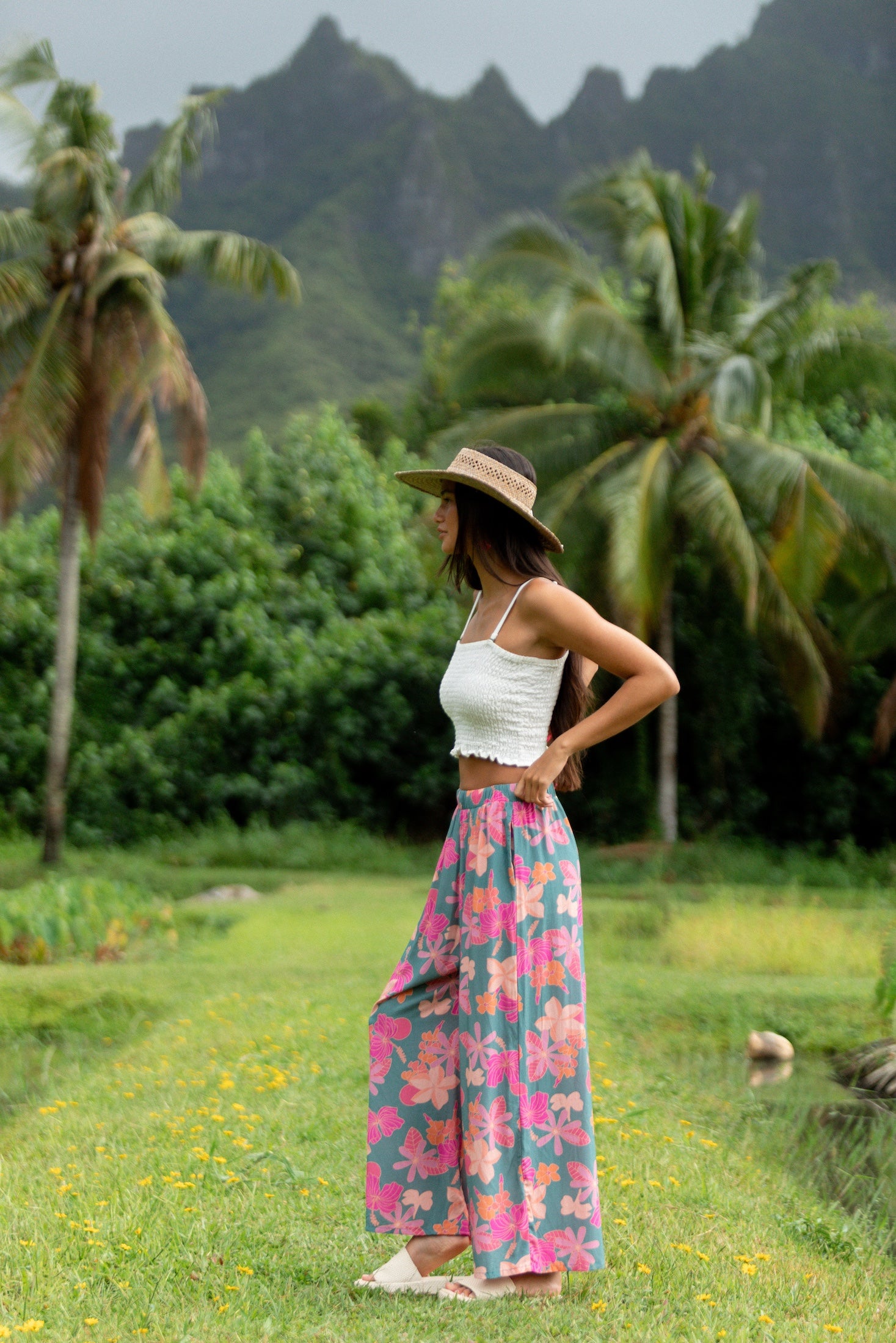 woman with brown hair wearing teal flowy pants with orange and pink foral print