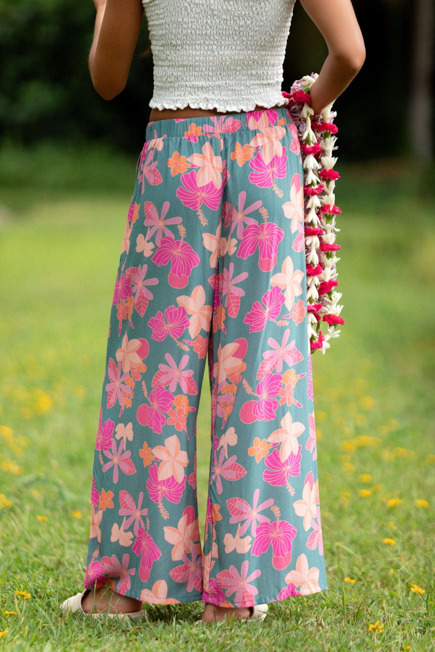 woman with brown hair wearing teal flowy pants with orange and pink foral print