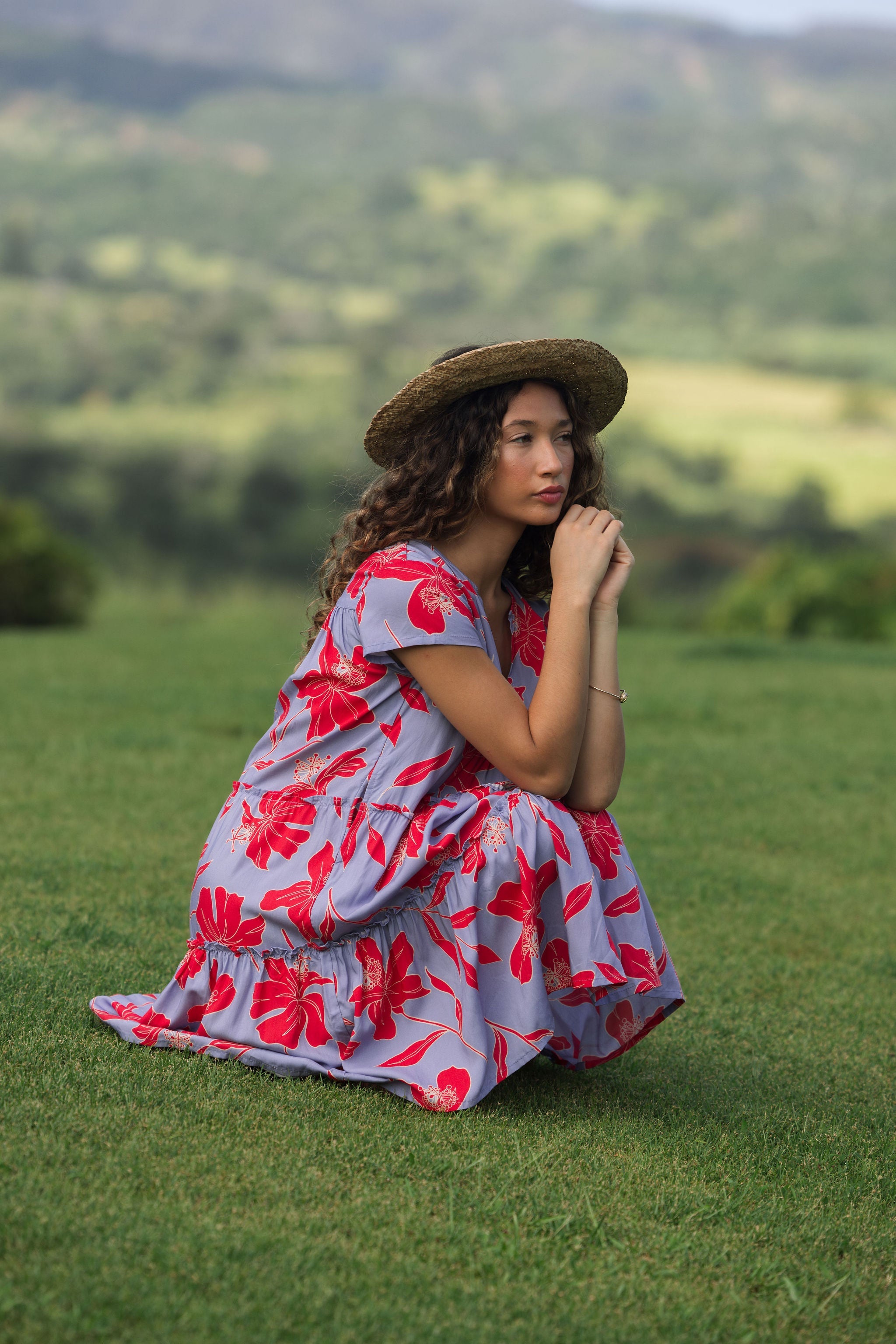 woman with brown hair wearing a flowy dress with periwinkle background and bright red hibiscus print.