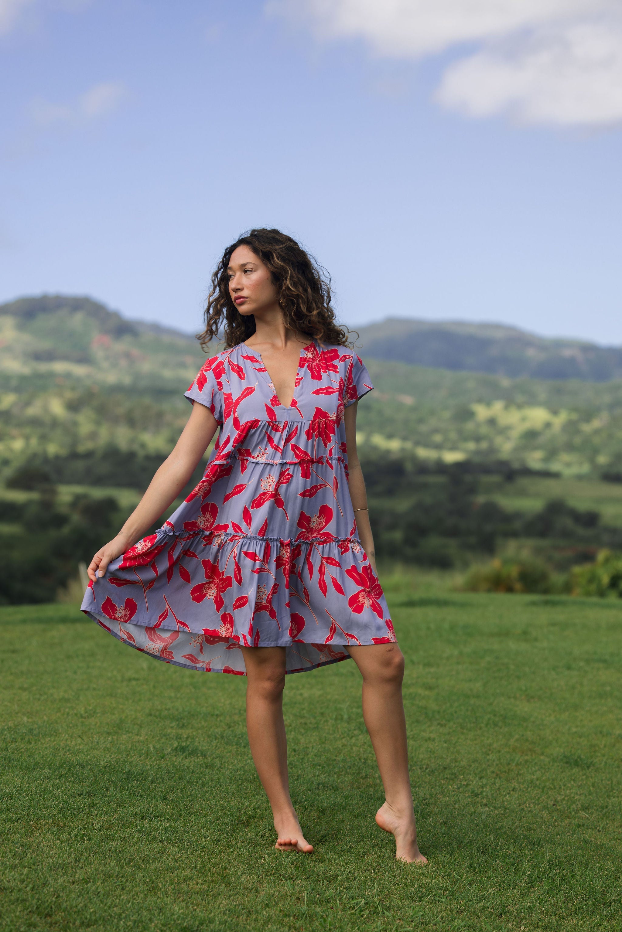 woman with brown hair wearing a flowy dress with periwinkle background and bright red hibiscus print.