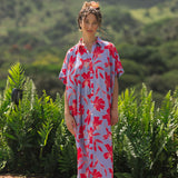 woman with brown hair wearing a maxi button up dress with periwinkle background and bright red hibiscus print.