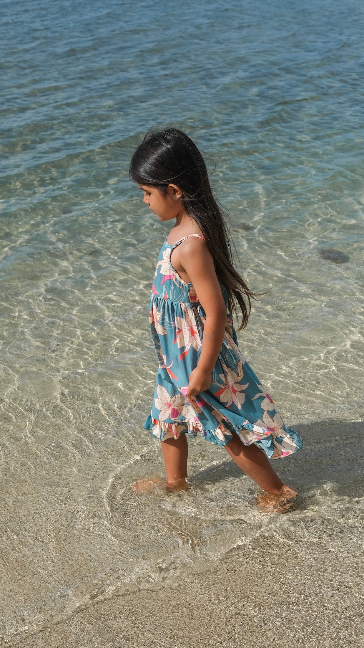 little girl wearing a teal flowy dress with cream colored orchid pattern
