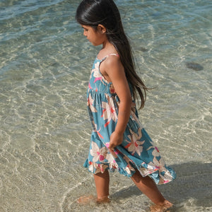 little girl wearing a teal flowy dress with cream colored orchid pattern