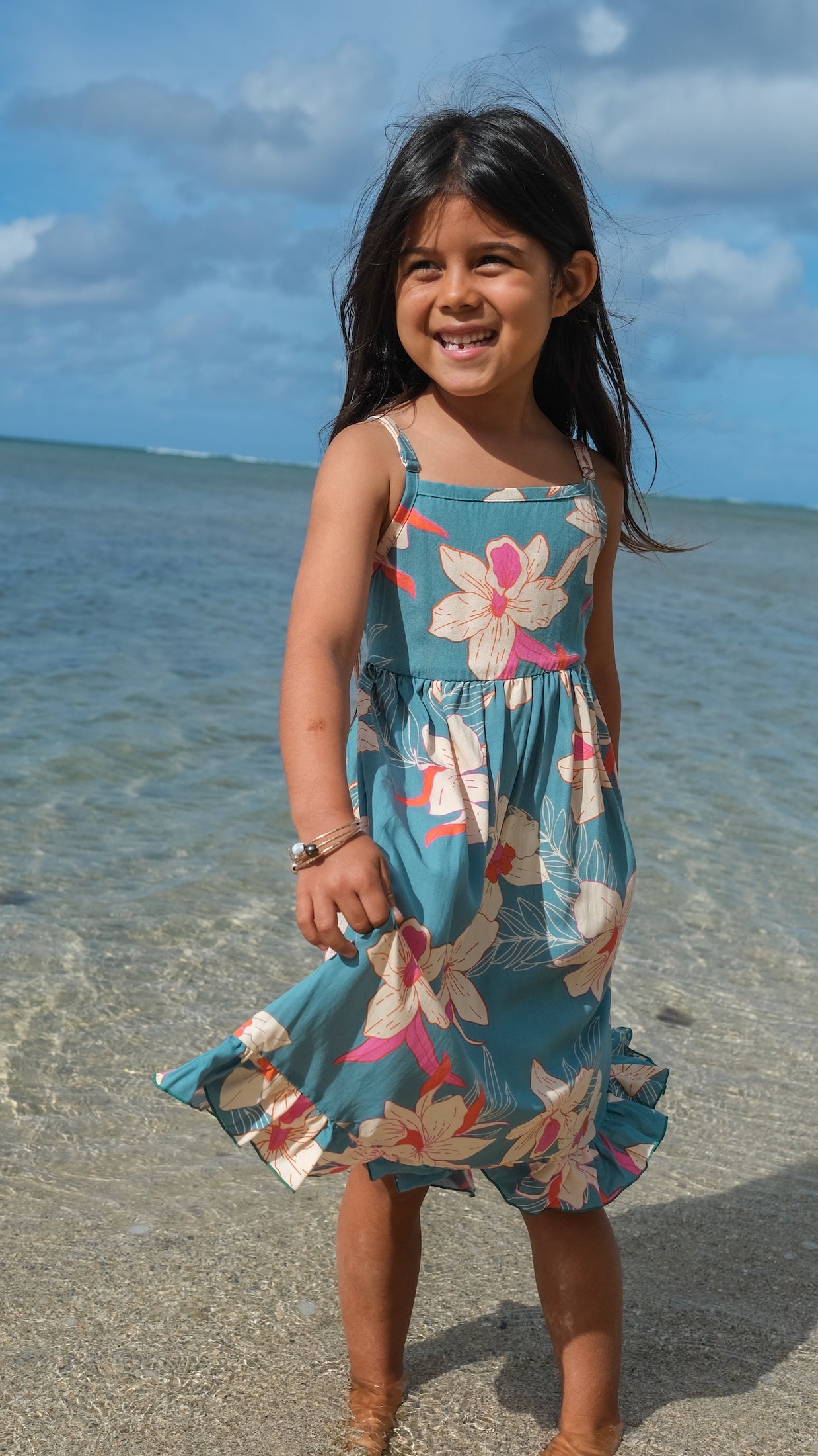 little girl wearing a teal flowy dress with cream colored orchid pattern