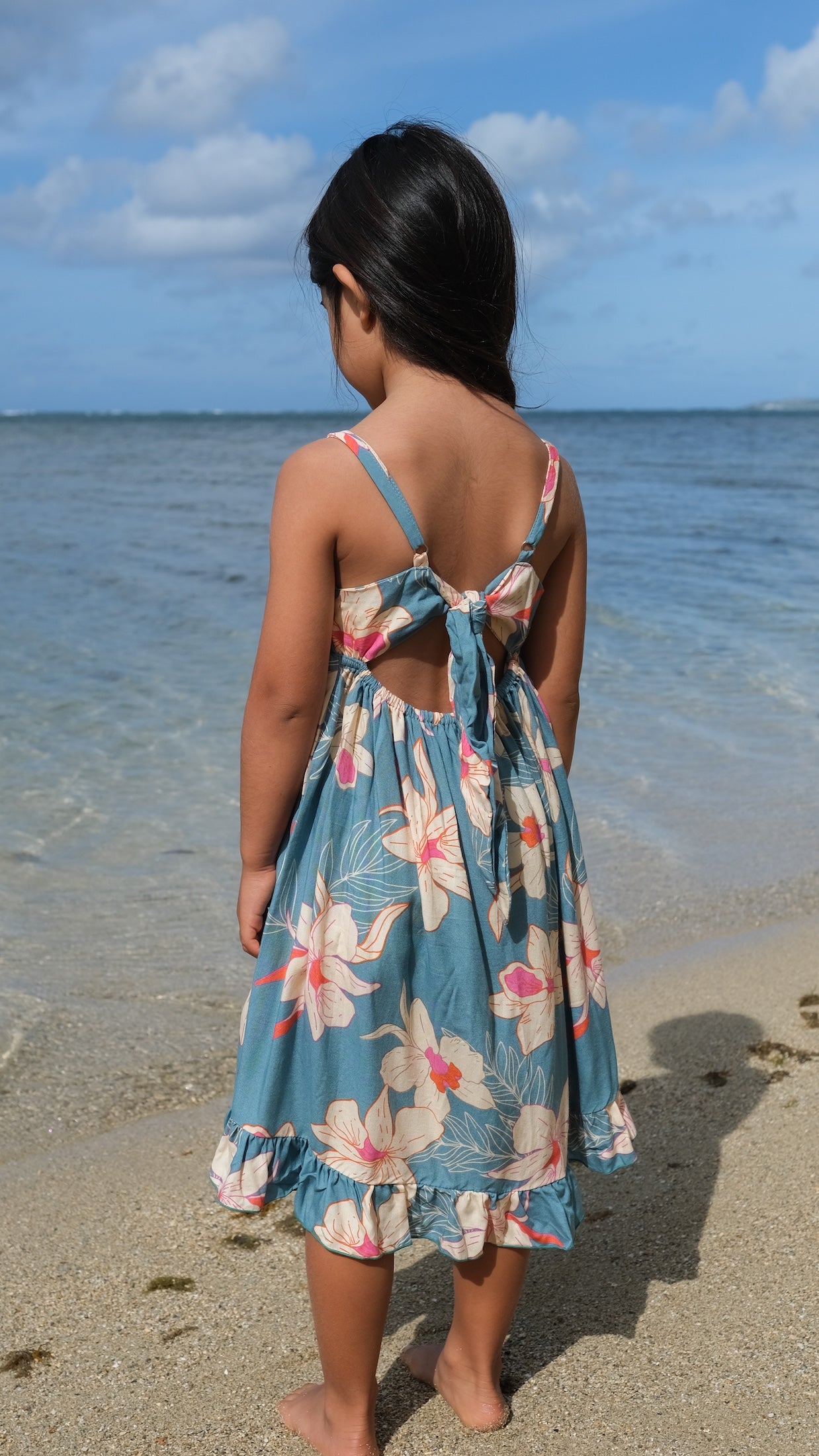 little girl wearing a teal flowy dress with cream colored orchid pattern