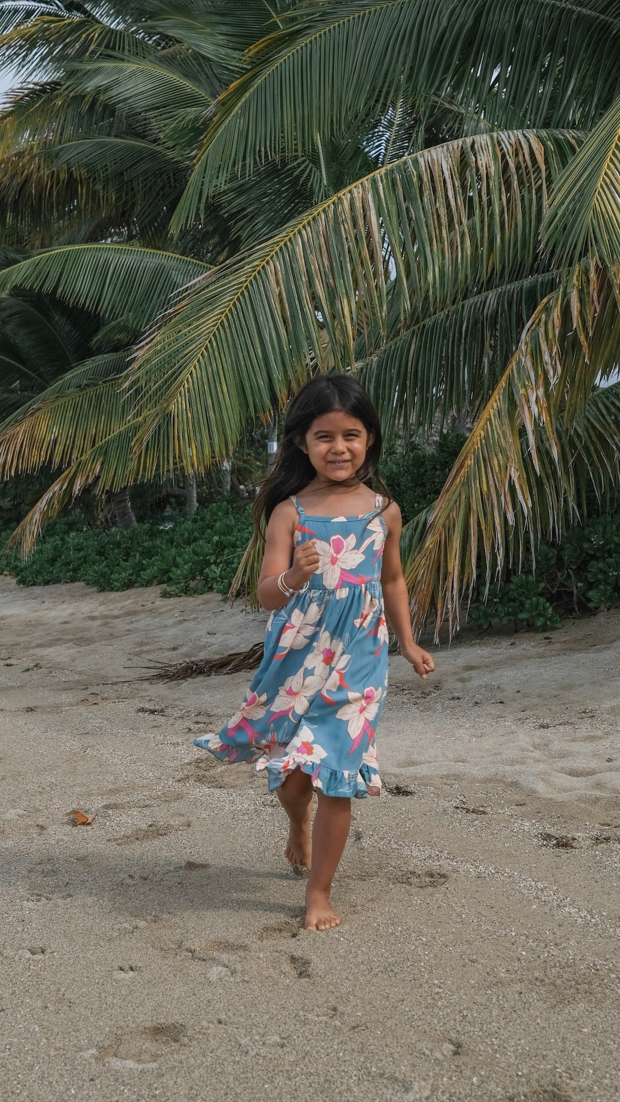 little girl wearing a teal flowy dress with cream colored orchid pattern