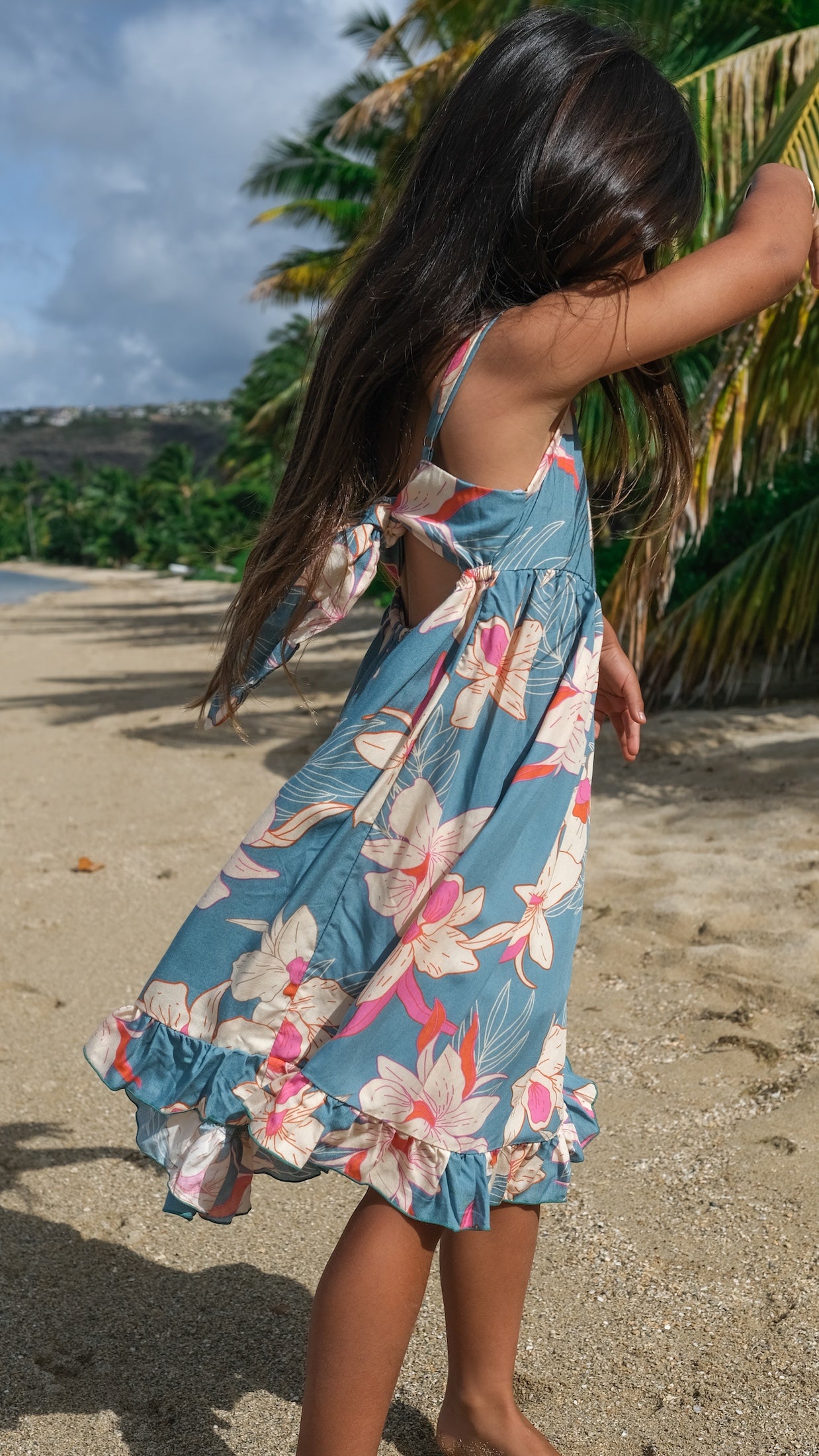 little girl wearing a teal flowy dress with cream colored orchid pattern