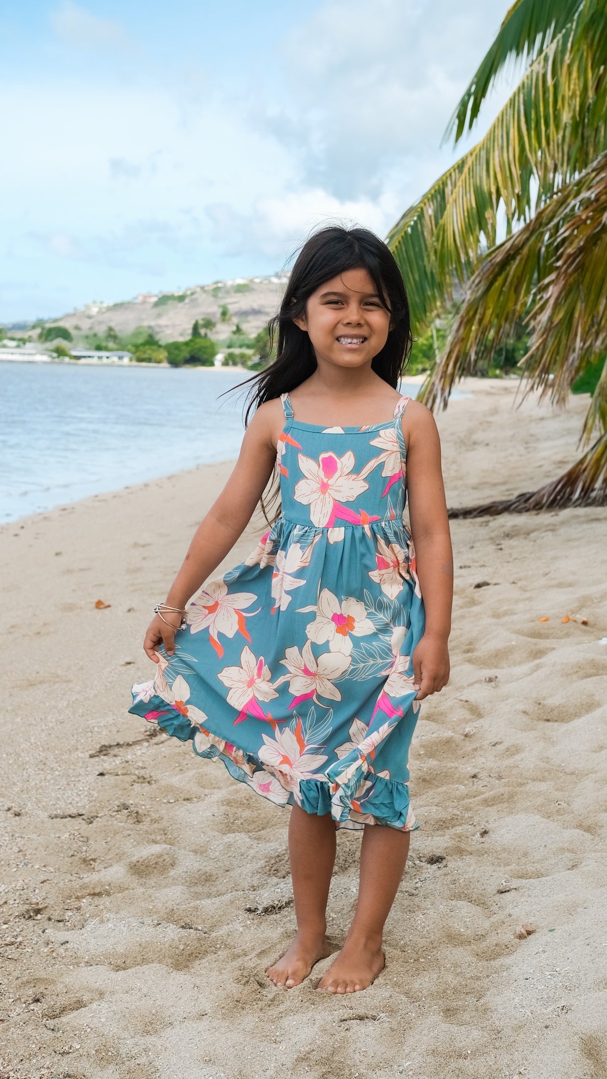 little girl wearing a teal flowy dress with cream colored orchid pattern