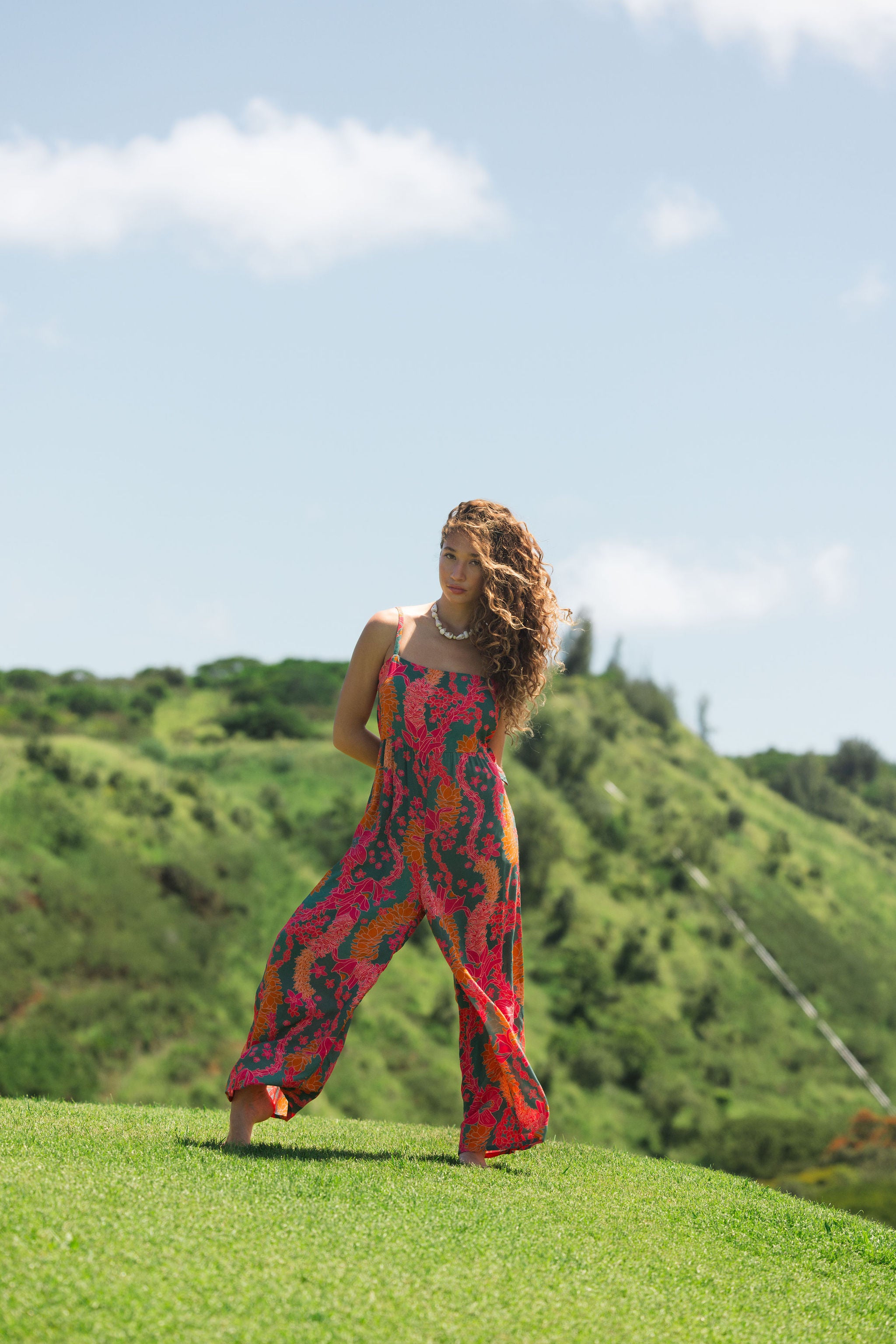 woman with brown hair wearing a colorful jumpsuit with tropical lei print