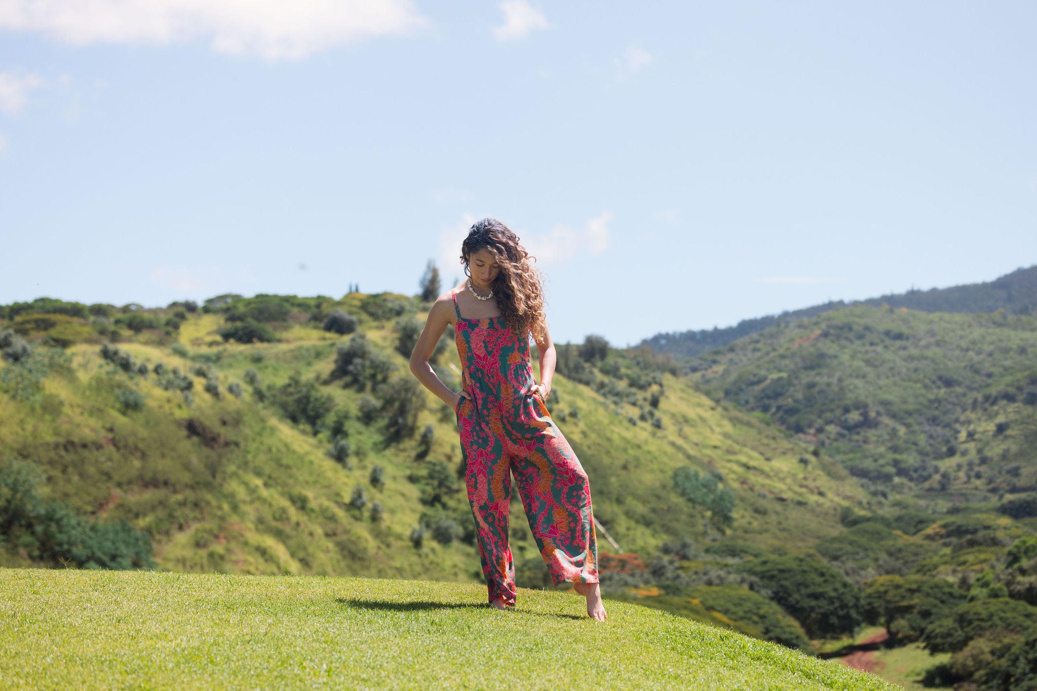 woman with brown hair wearing a colorful jumpsuit with tropical lei print