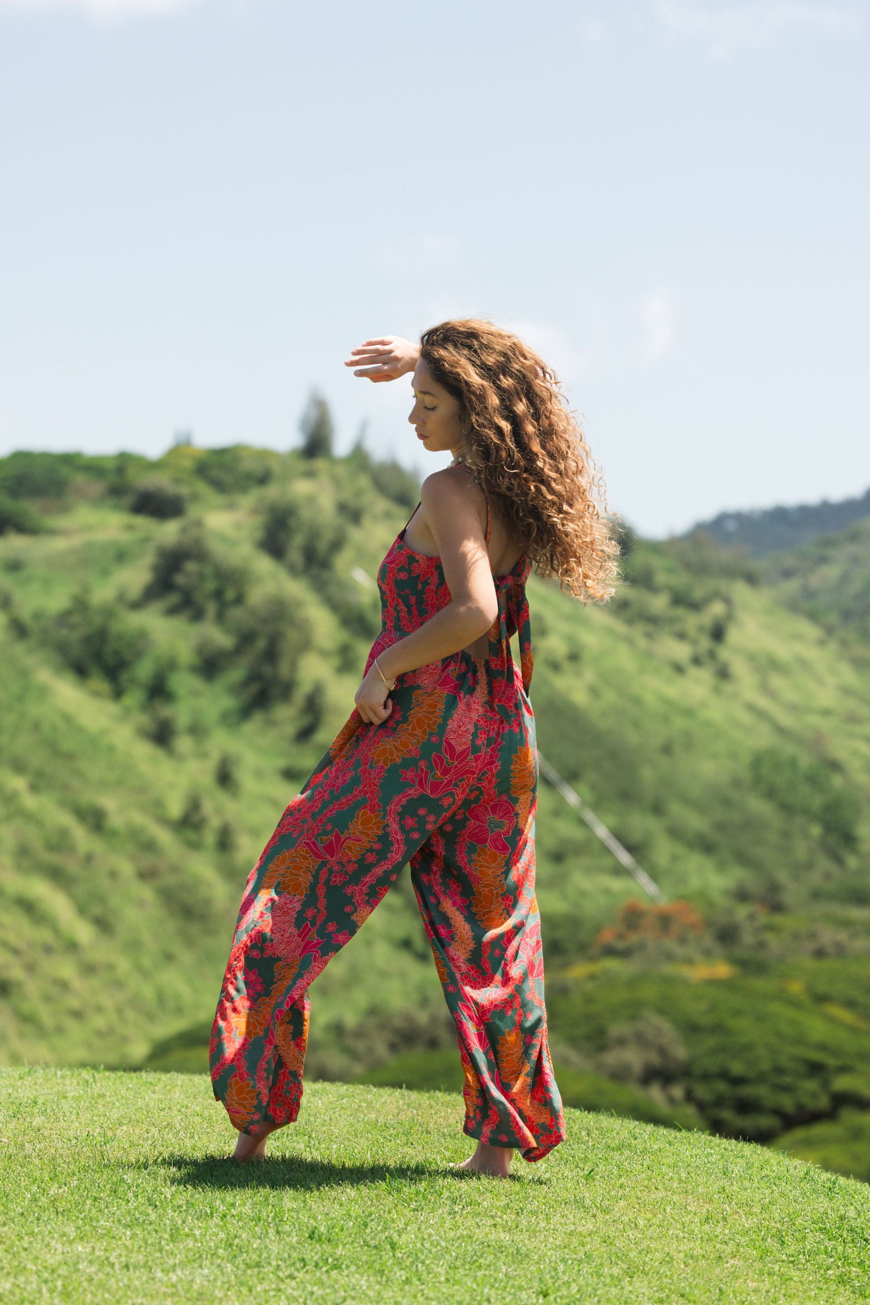 woman with brown hair wearing a colorful jumpsuit with tropical lei print