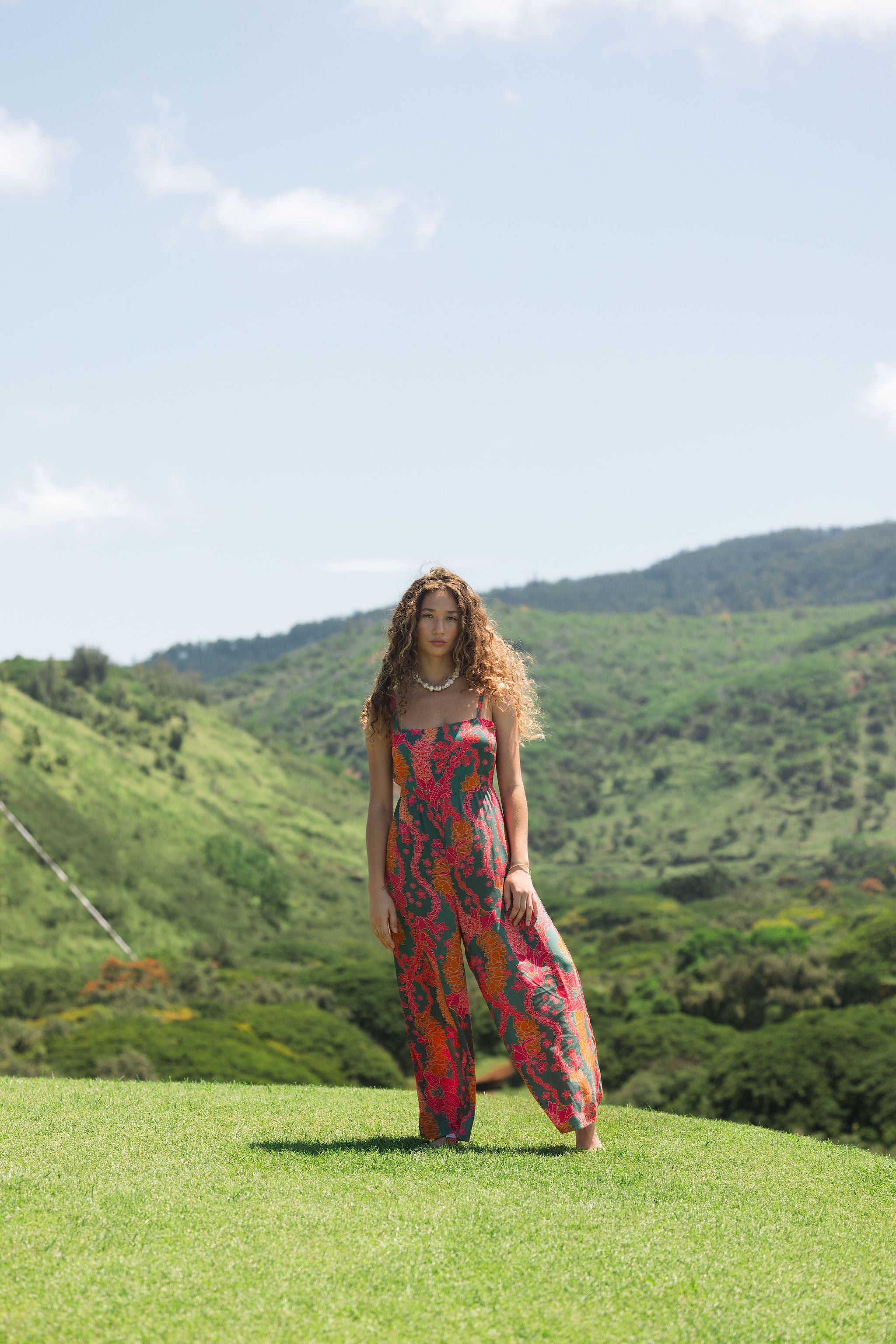 woman with brown hair wearing a colorful jumpsuit with tropical lei print