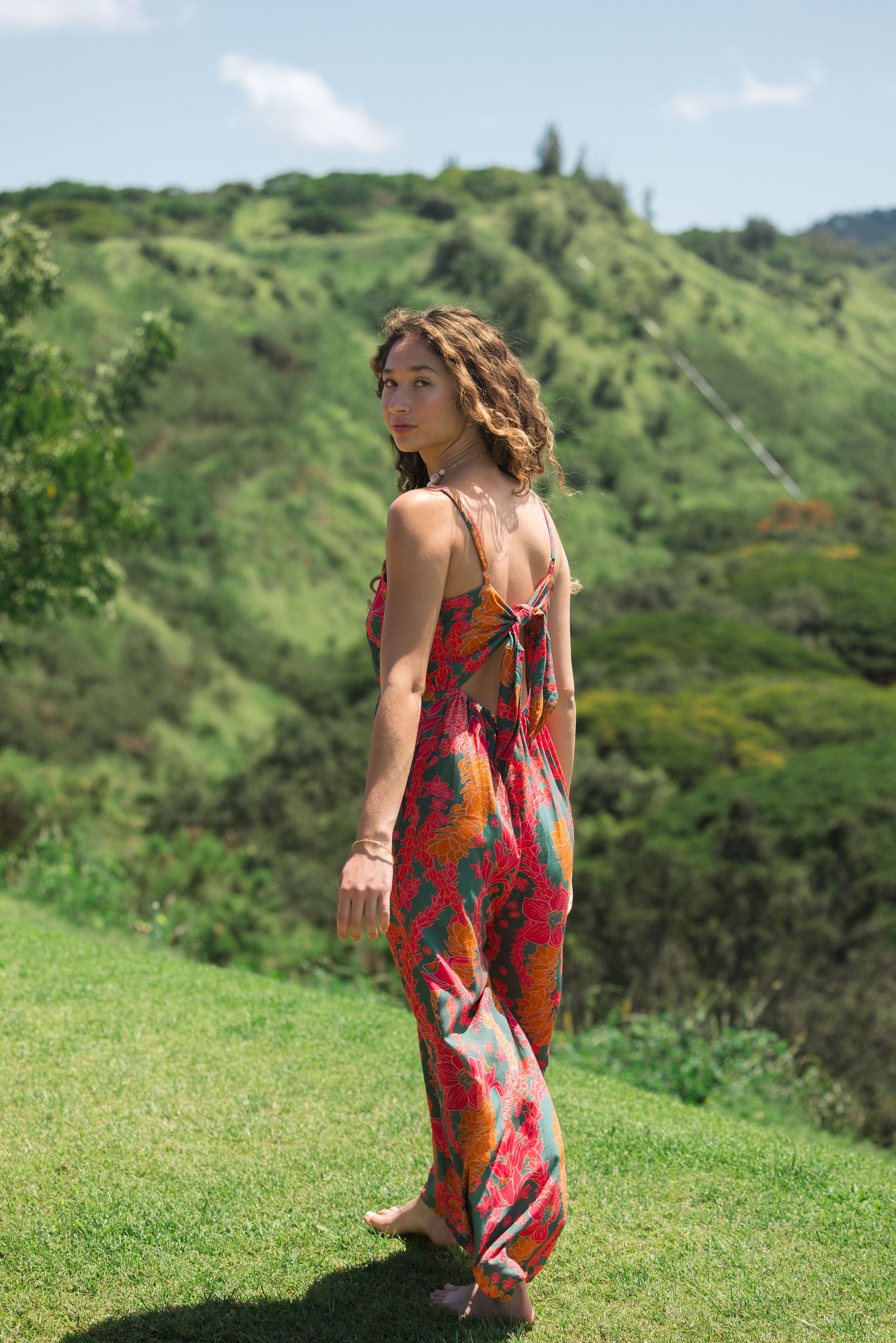 woman with brown hair wearing a colorful jumpsuit with tropical lei print