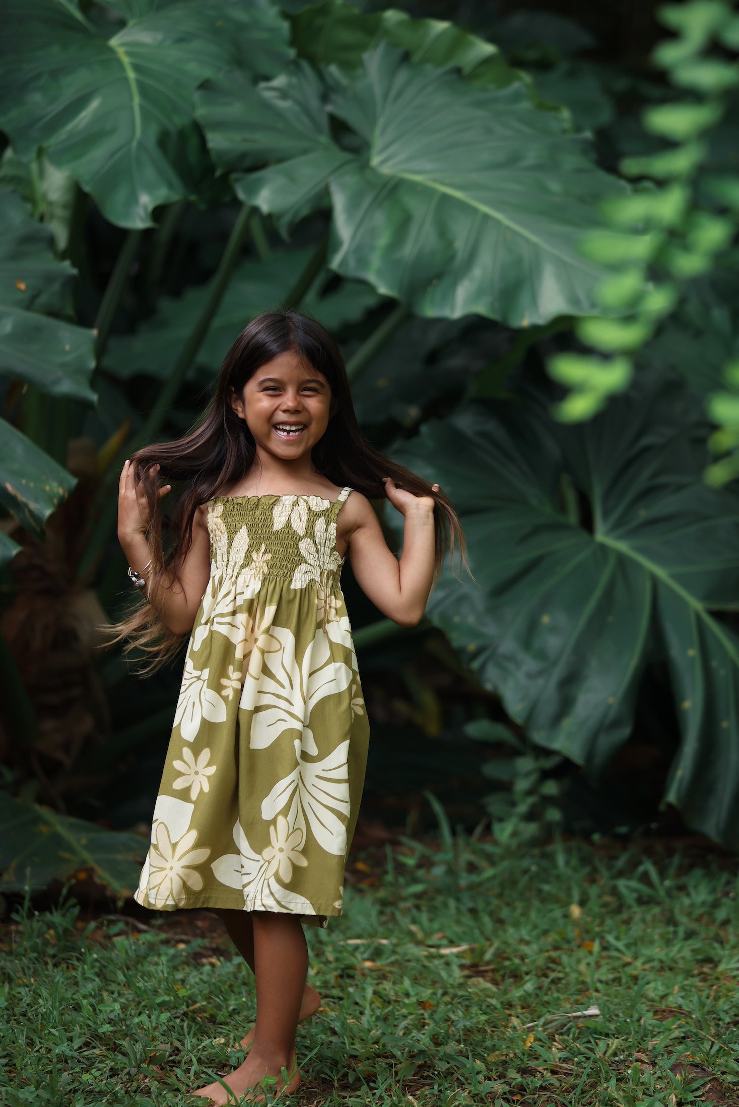 little girl wearing spaghetti strap dress in green print with naupaka pattern
