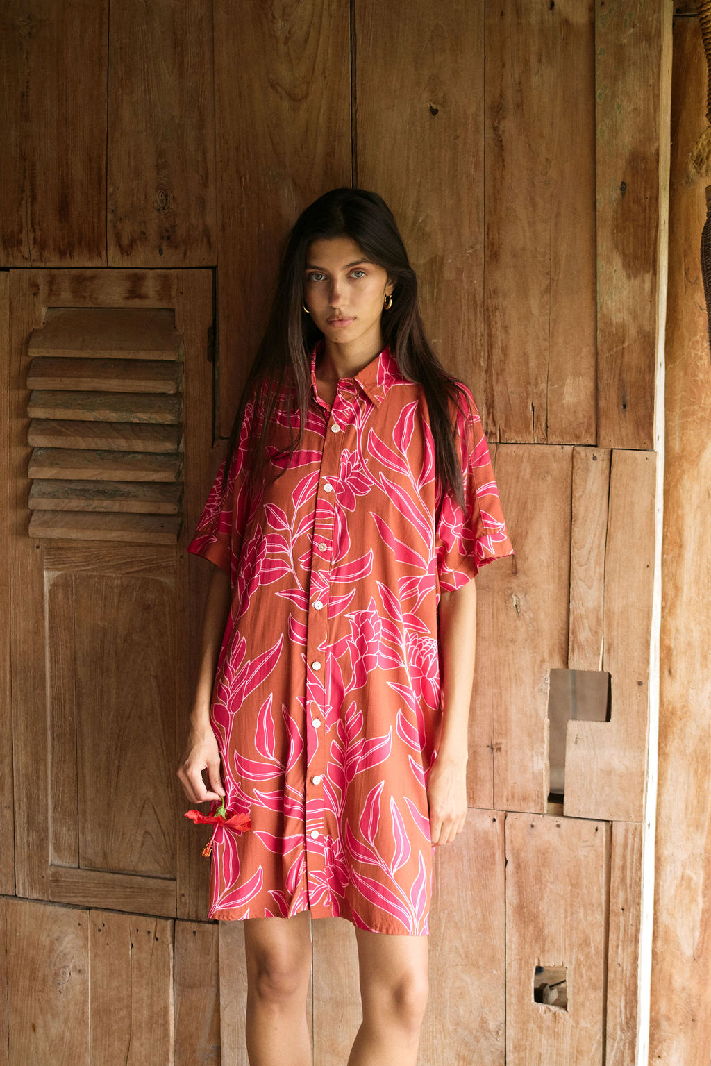 A woman with dark hair wears a YIREH collared, button-up dress. It is the Kaimana Dress in the Garden 'Awapuhi print.