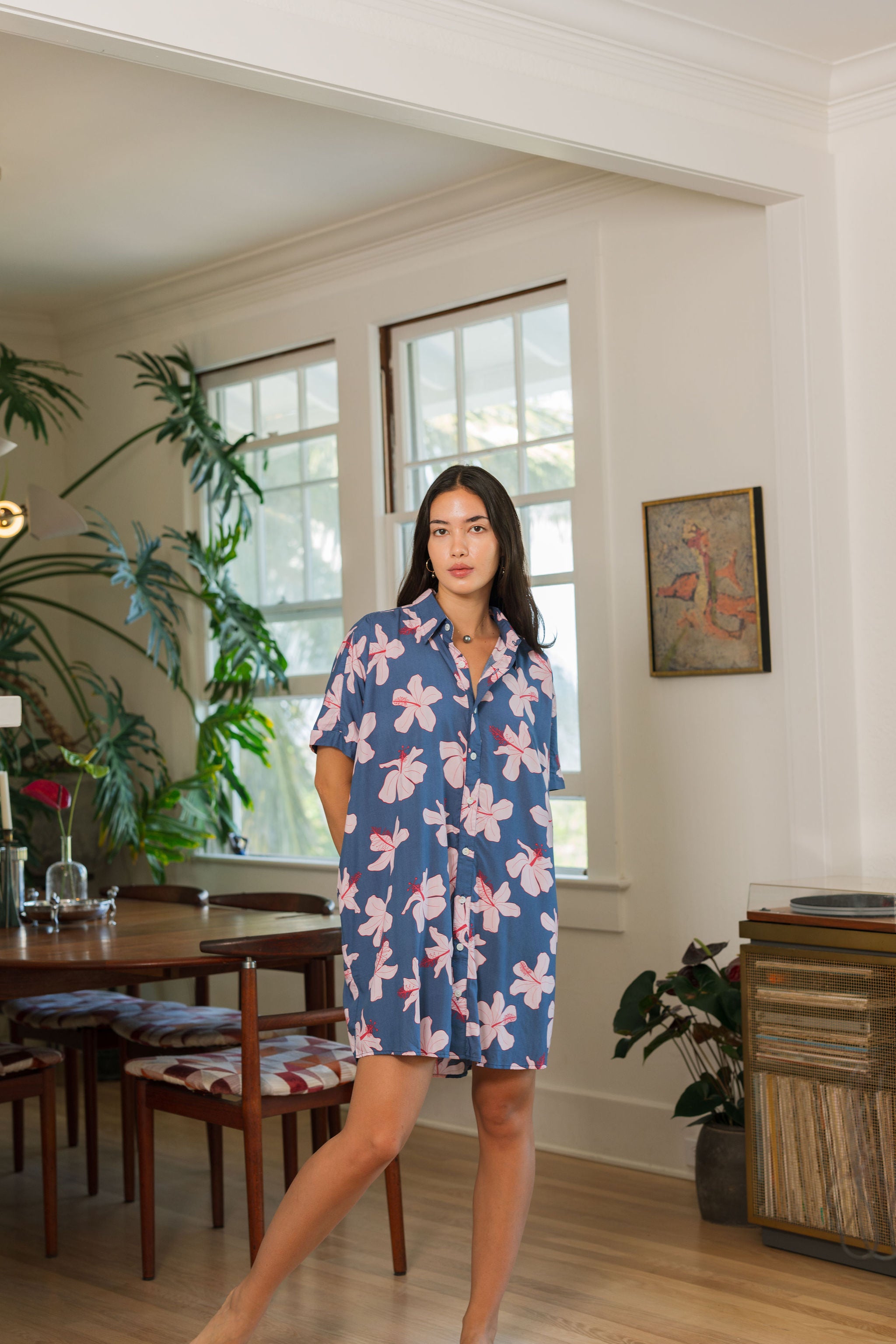 woman with black hair wearing a button up dress in a navy color with pink hibiscus blossoms