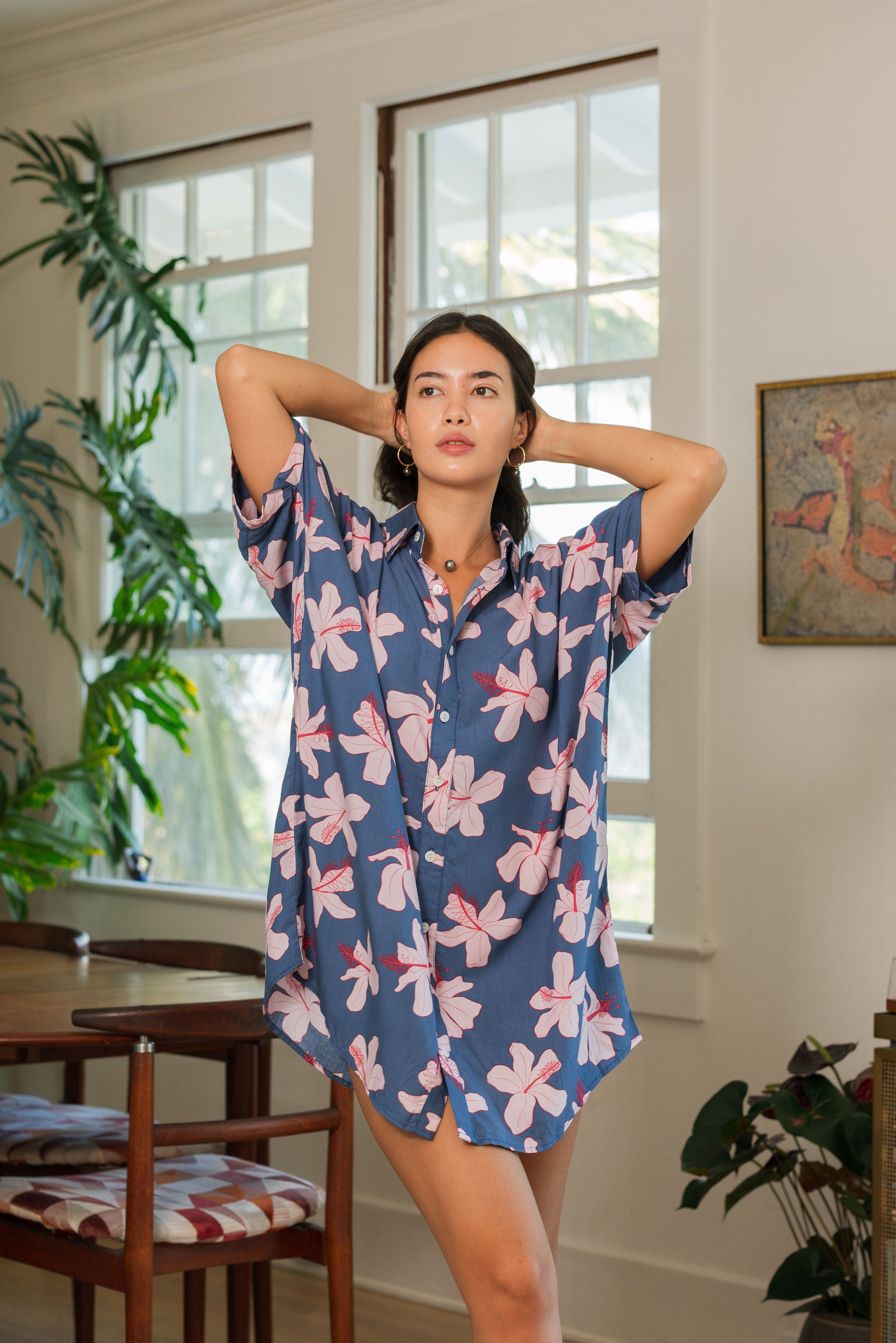 woman with black hair wearing a button up dress in a navy color with pink hibiscus blossoms
