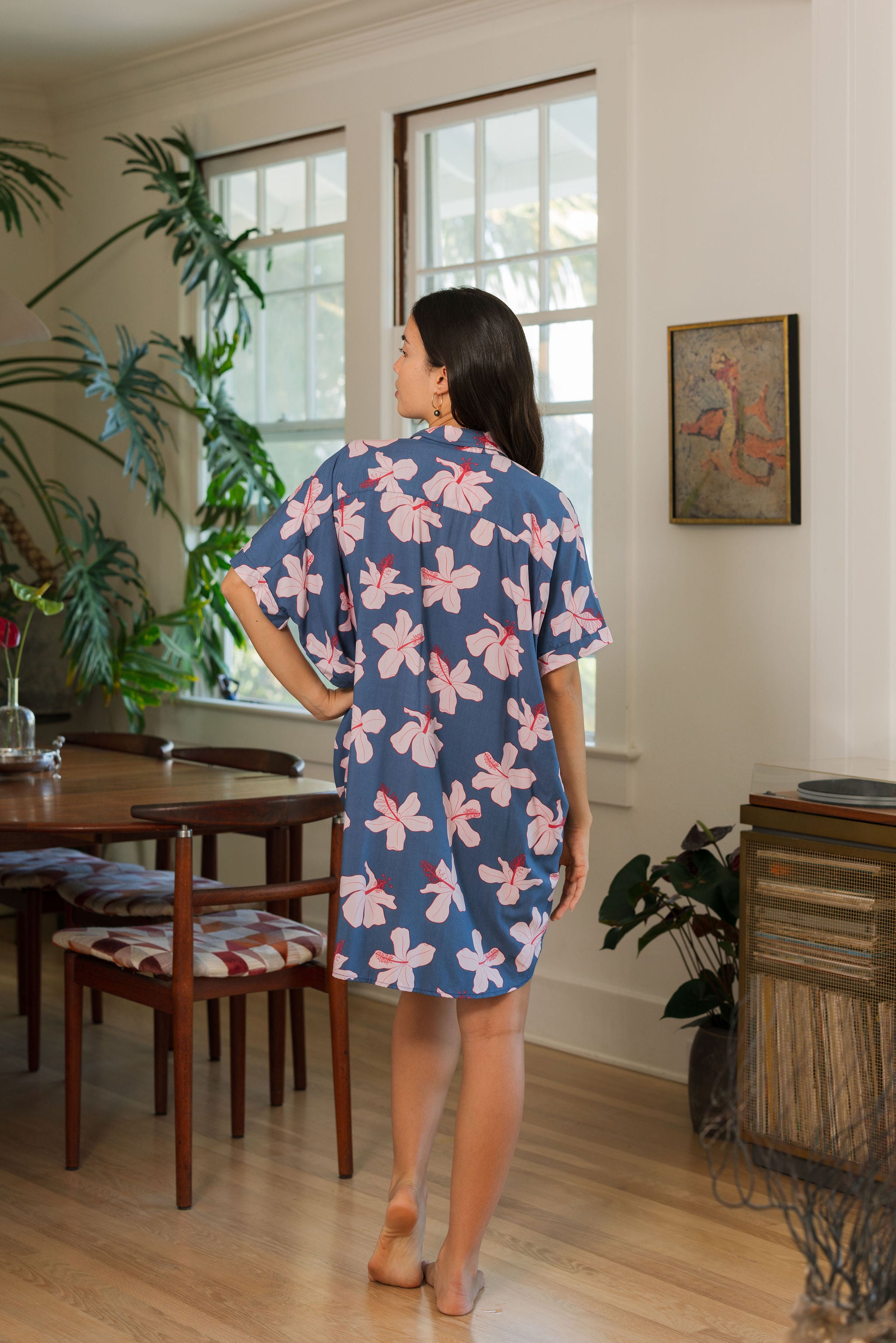 woman with black hair wearing a button up dress in a navy color with pink hibiscus blossoms