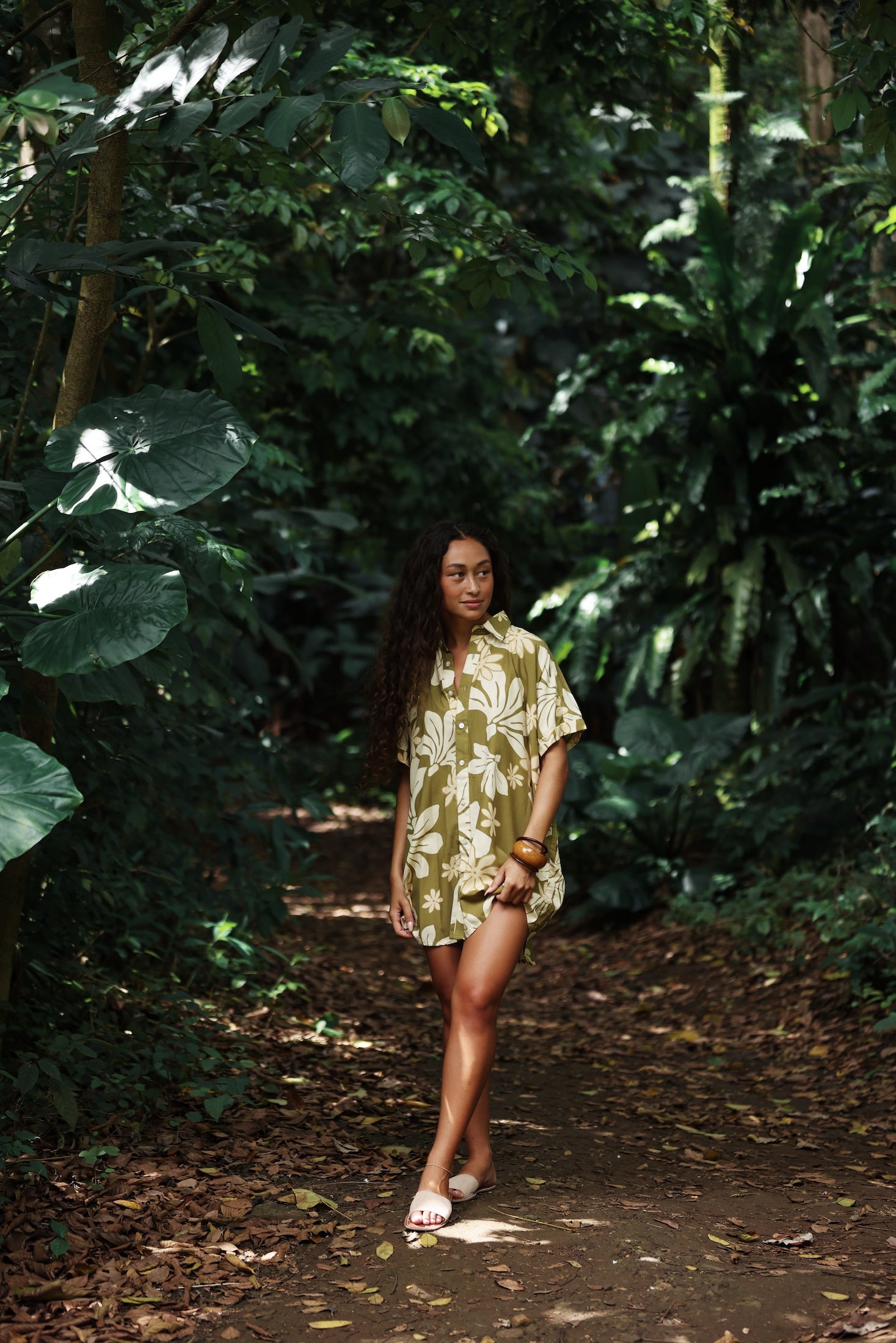 woman with brown hair wearing a button up dress in a green color with naupaka pattern throughout.
