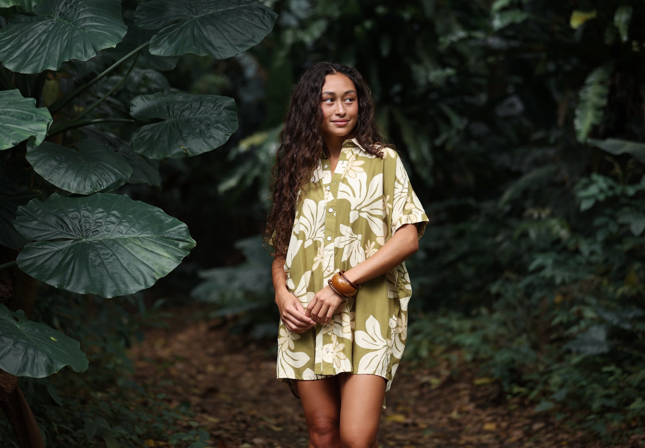 woman with brown hair wearing a button up dress in a green color with naupaka pattern throughout.