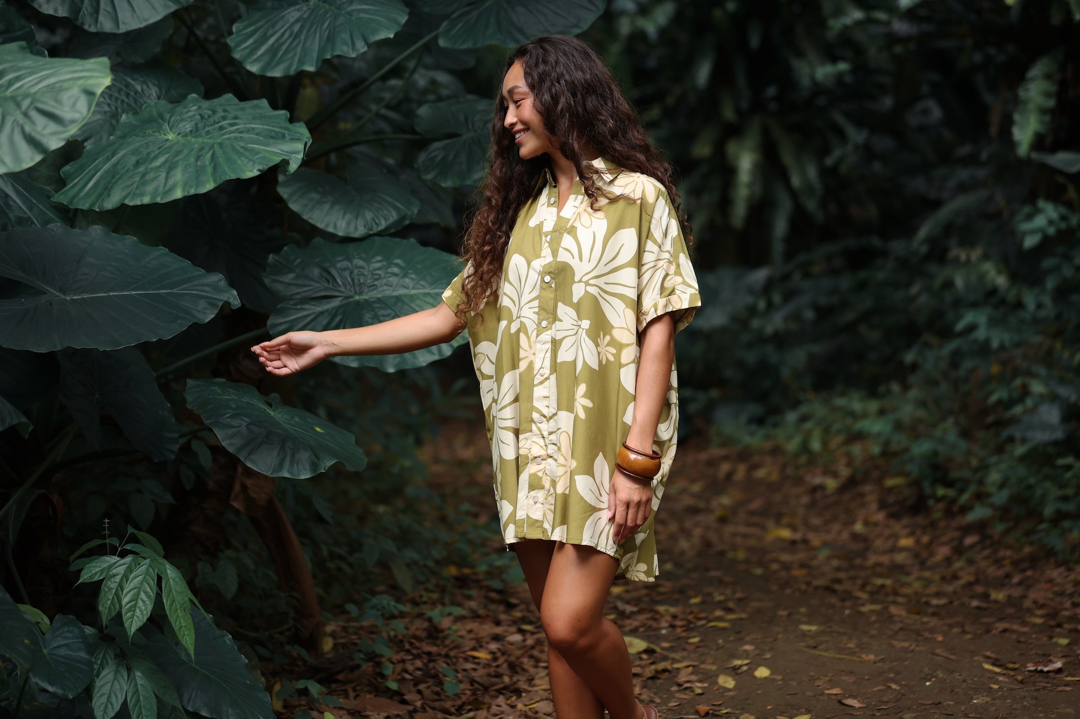 woman with brown hair wearing a button up dress in a green color with naupaka pattern throughout.