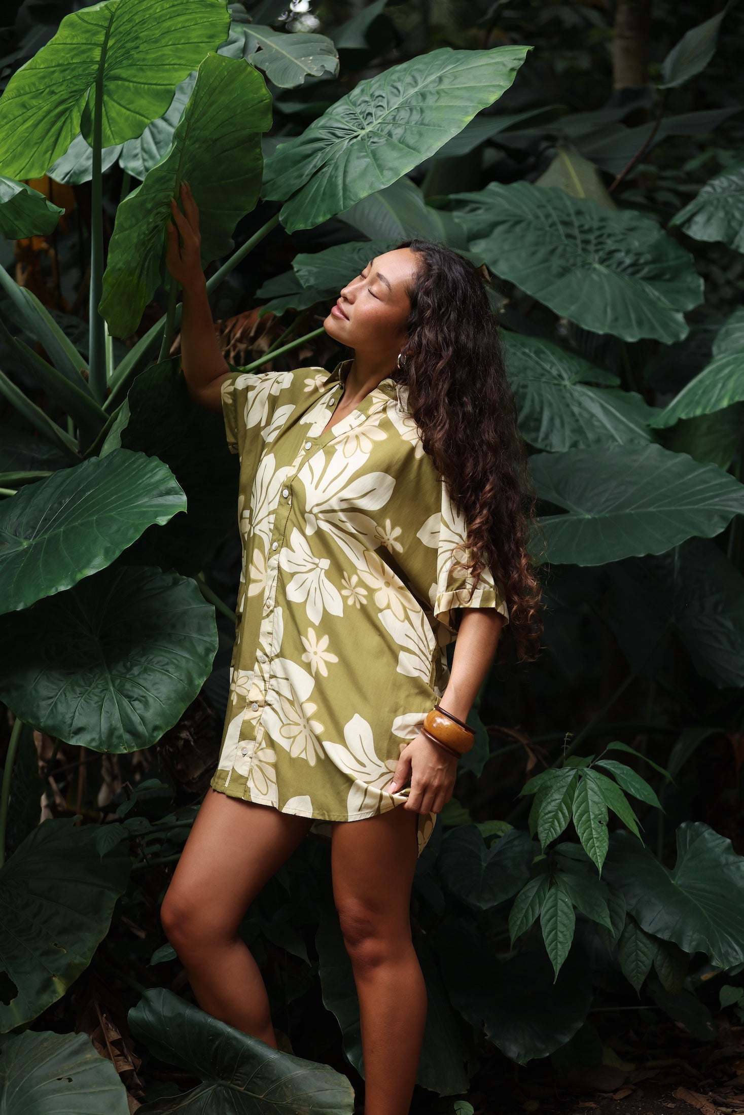 woman with brown hair wearing a button up dress in a green color with naupaka pattern throughout.