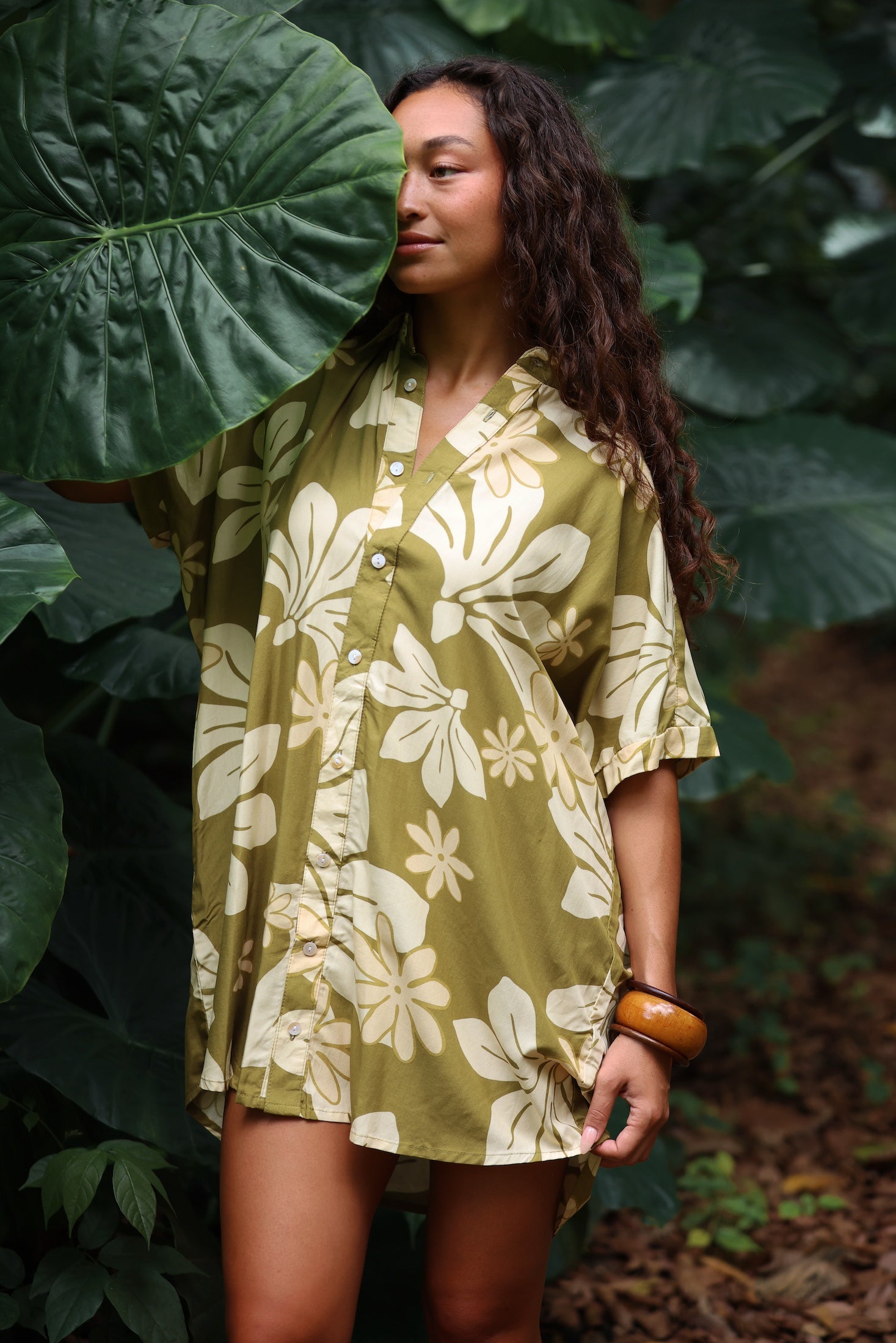 woman with brown hair wearing a button up dress in a green color with naupaka pattern throughout.