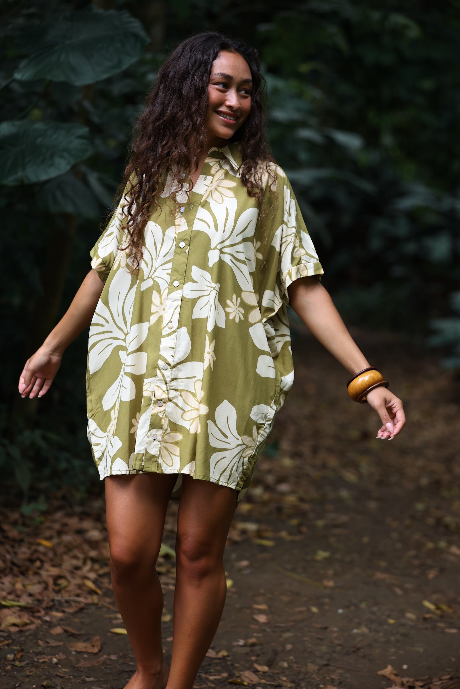 woman with brown hair wearing a button up dress in a green color with naupaka pattern throughout.
