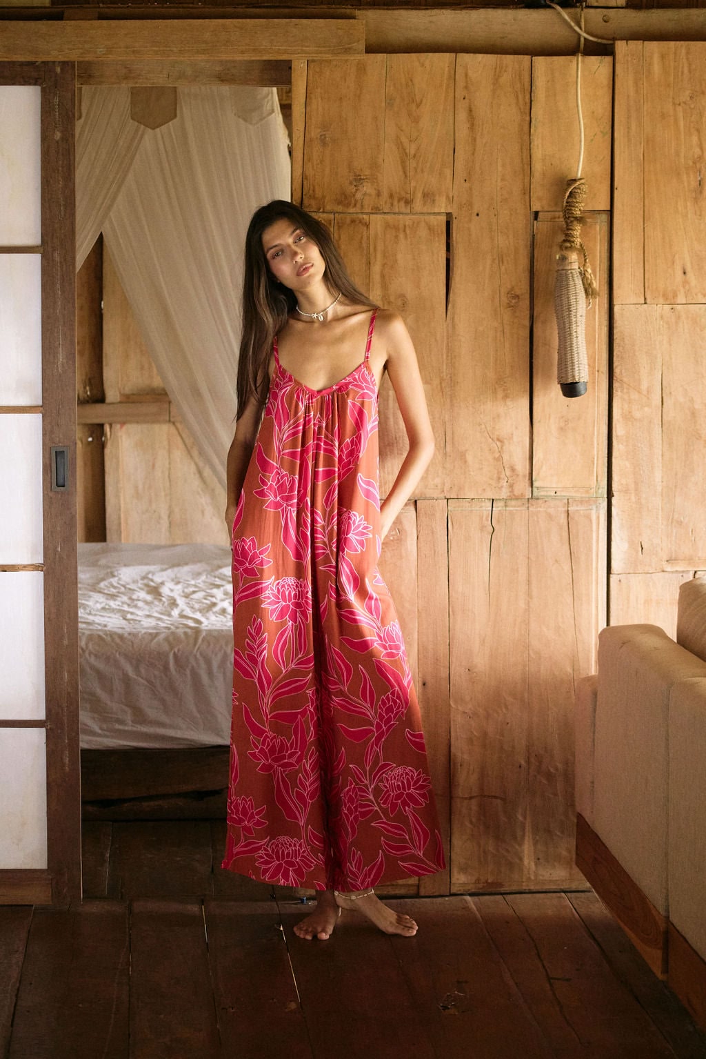 A woman with dark hair wears a YIREH v-neck, wide legged jumpsuit. It is the Laney Jumpsuit in the Garden 'Awapuhi print.