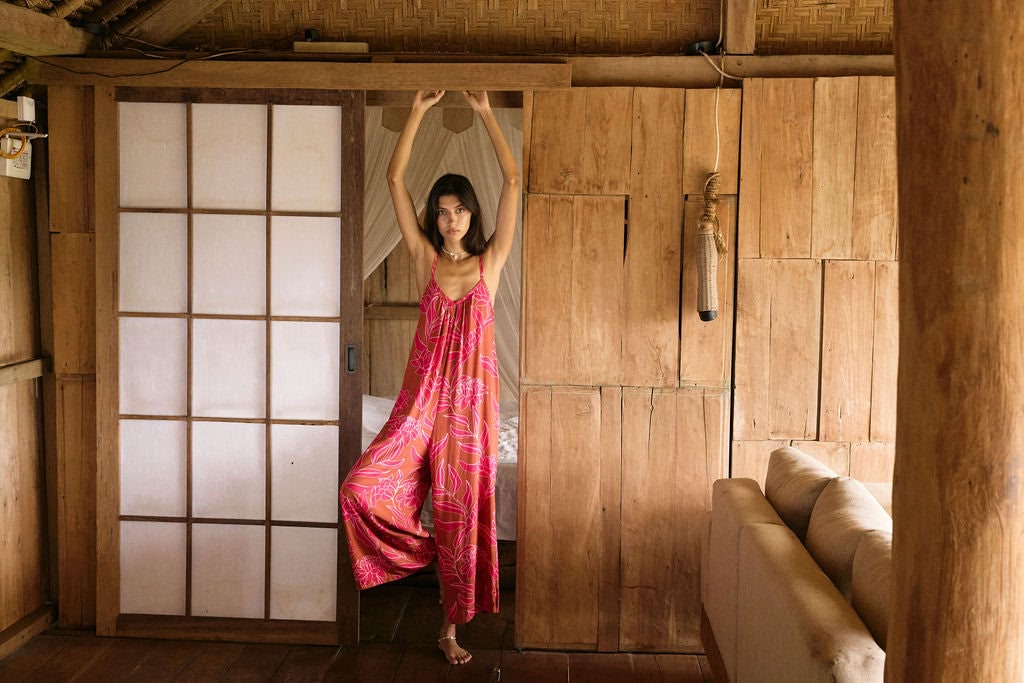 A woman with dark hair wears a YIREH v-neck, wide legged jumpsuit. It is the Laney Jumpsuit in the Garden 'Awapuhi print.