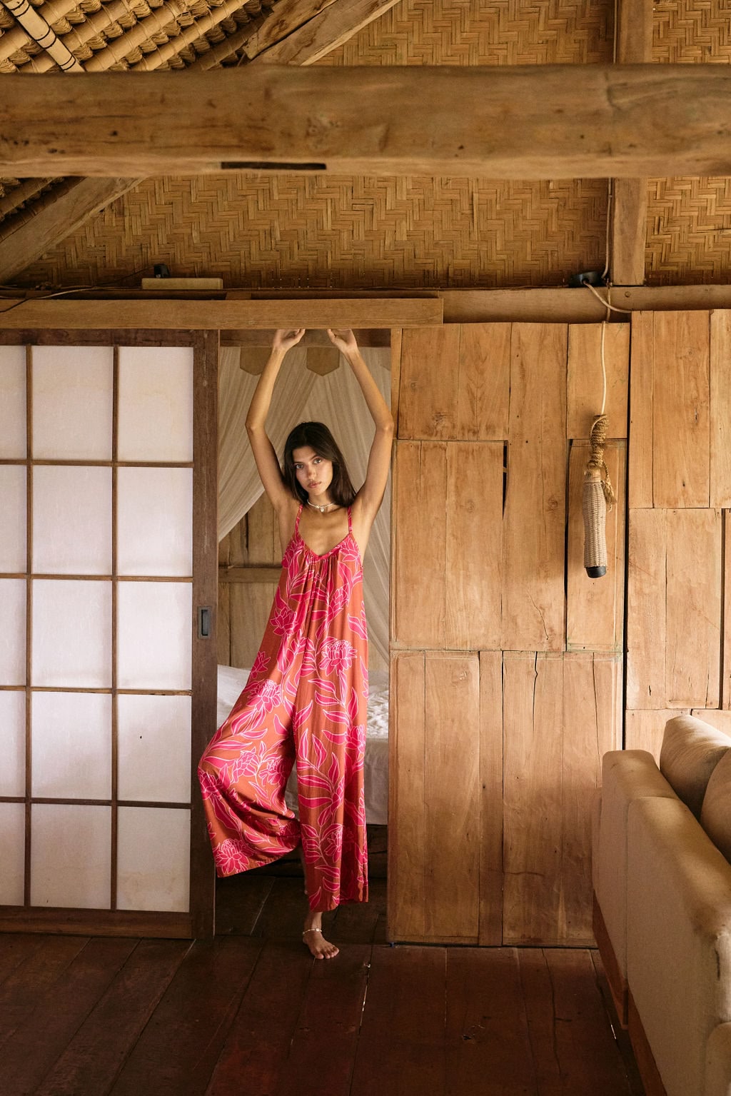 A woman with dark hair wears a YIREH v-neck, wide legged jumpsuit. It is the Laney Jumpsuit in the Garden 'Awapuhi print.