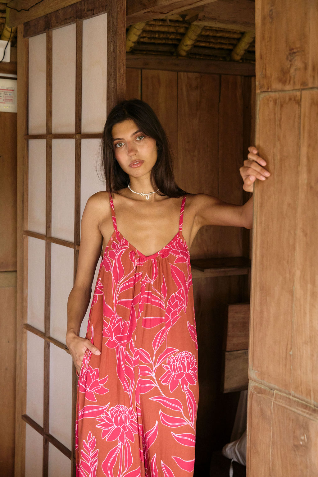 A woman with dark hair wears a YIREH v-neck, wide legged jumpsuit. It is the Laney Jumpsuit in the Garden 'Awapuhi print.