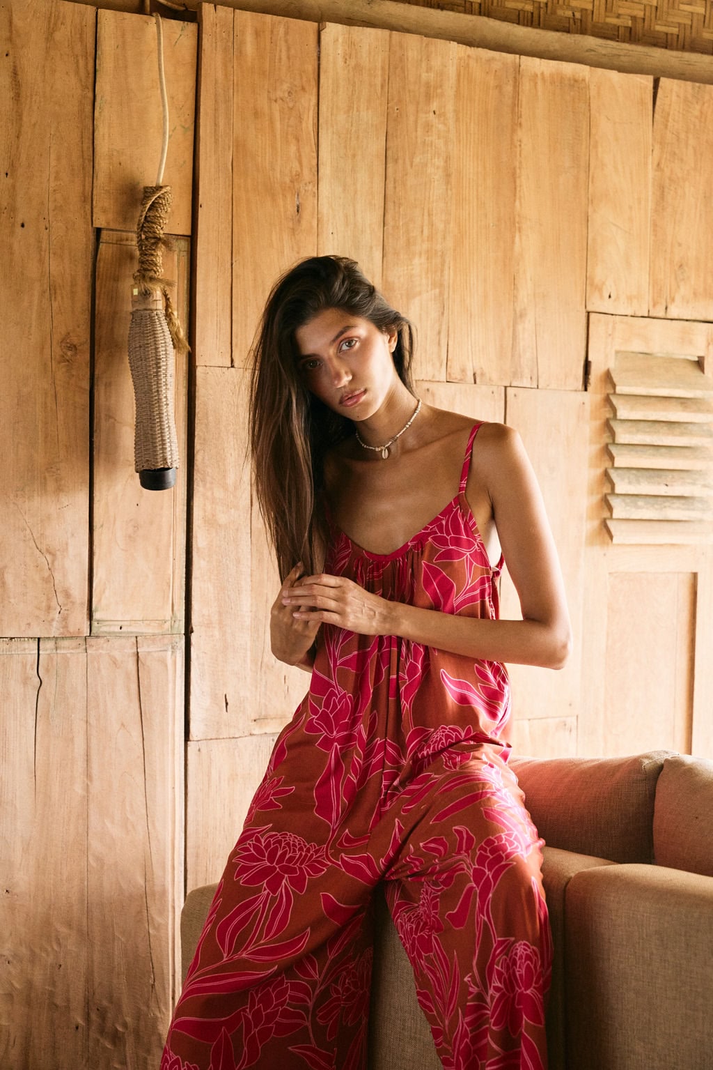 A woman with dark hair wears a YIREH v-neck, wide legged jumpsuit. It is the Laney Jumpsuit in the Garden 'Awapuhi print.