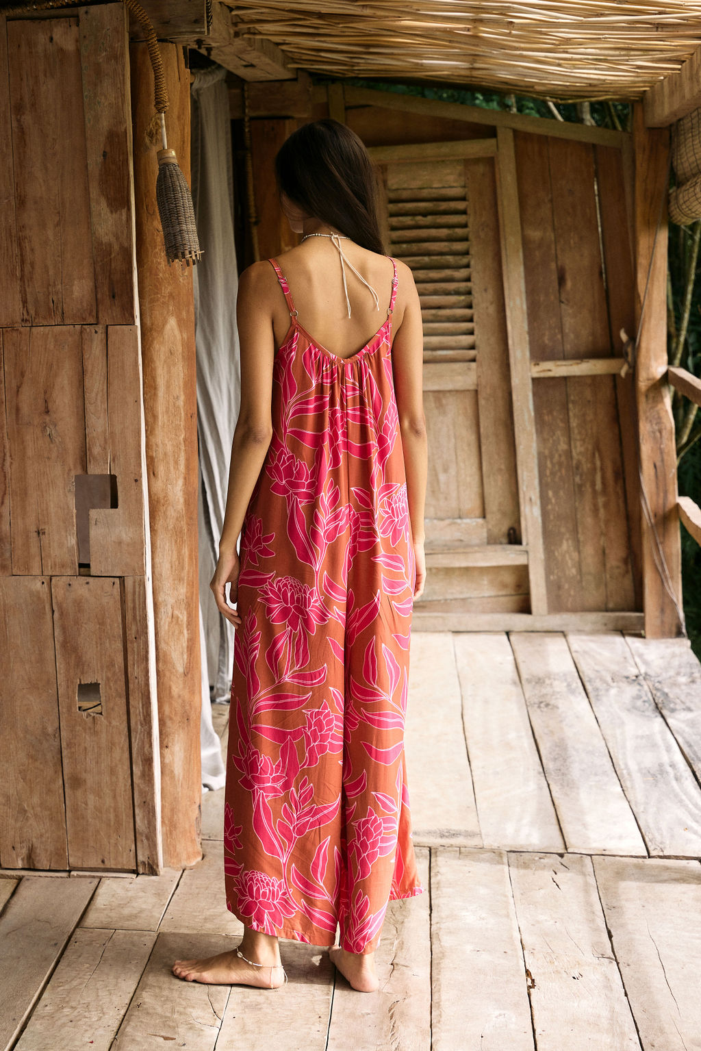 A woman with dark hair wears a YIREH v-neck, wide legged jumpsuit. It is the Laney Jumpsuit in the Garden 'Awapuhi print.