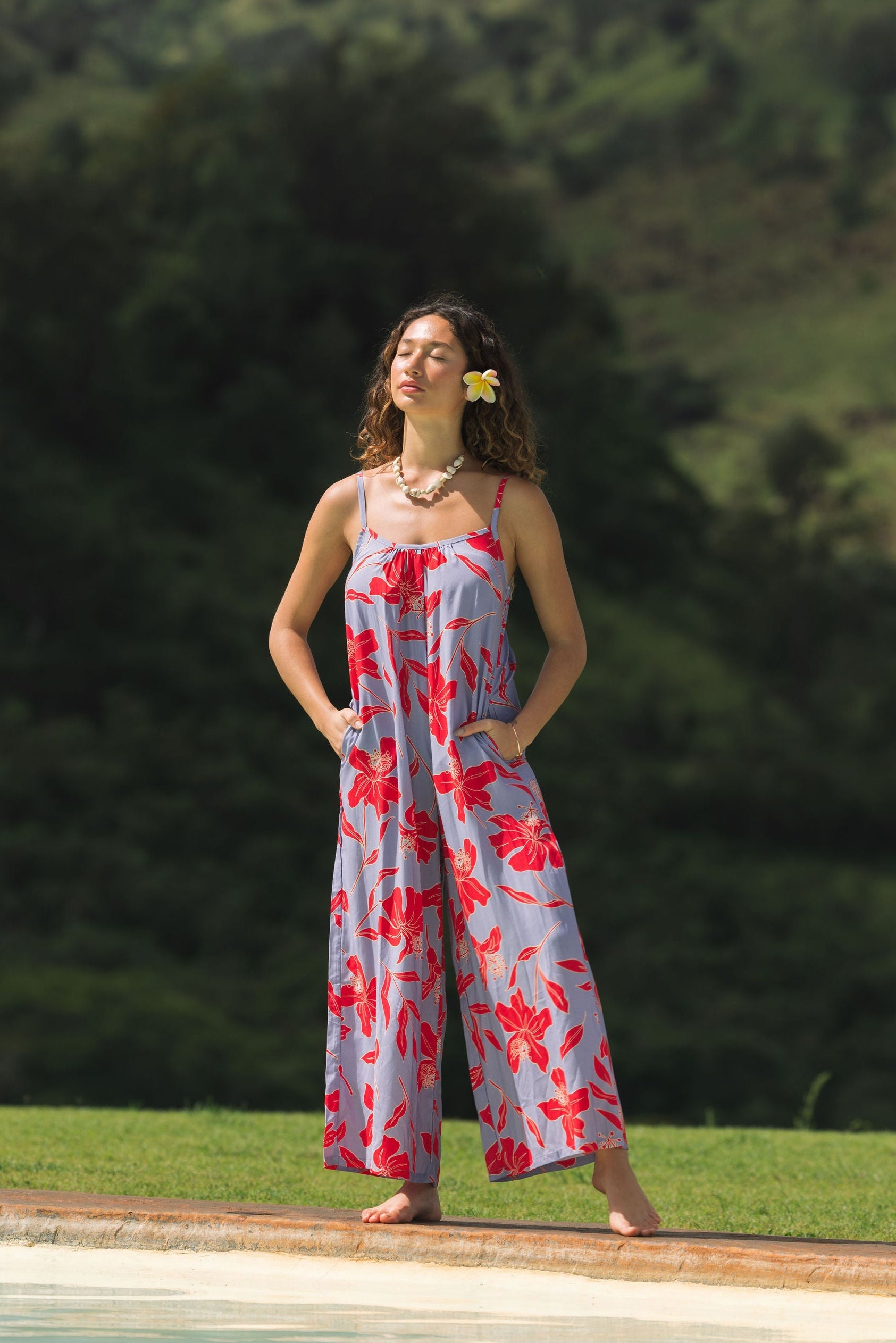 woman with brown hair wearing a jumpsuit with periwinkle background and bright red hibiscus print.
