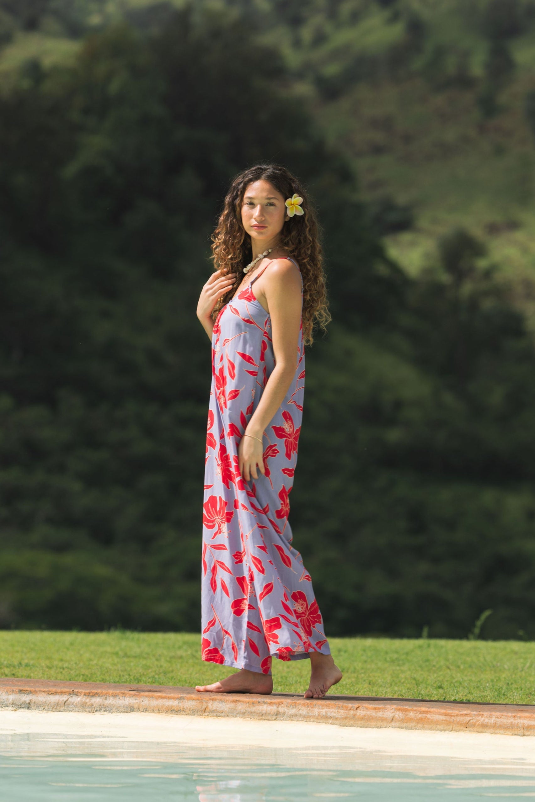 woman with brown hair wearing a jumpsuit with periwinkle background and bright red hibiscus print.