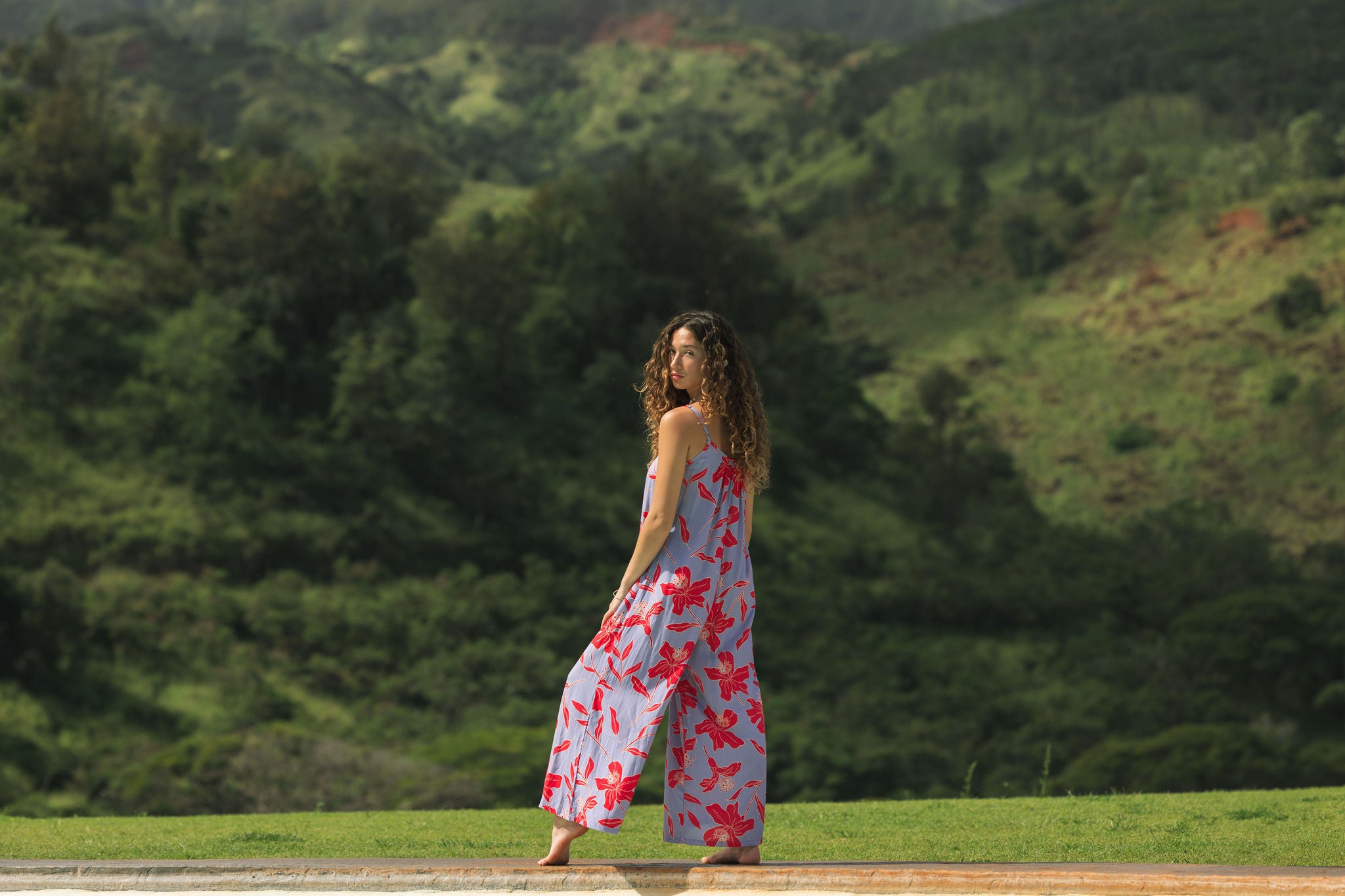 woman with brown hair wearing a jumpsuit with periwinkle background and bright red hibiscus print.