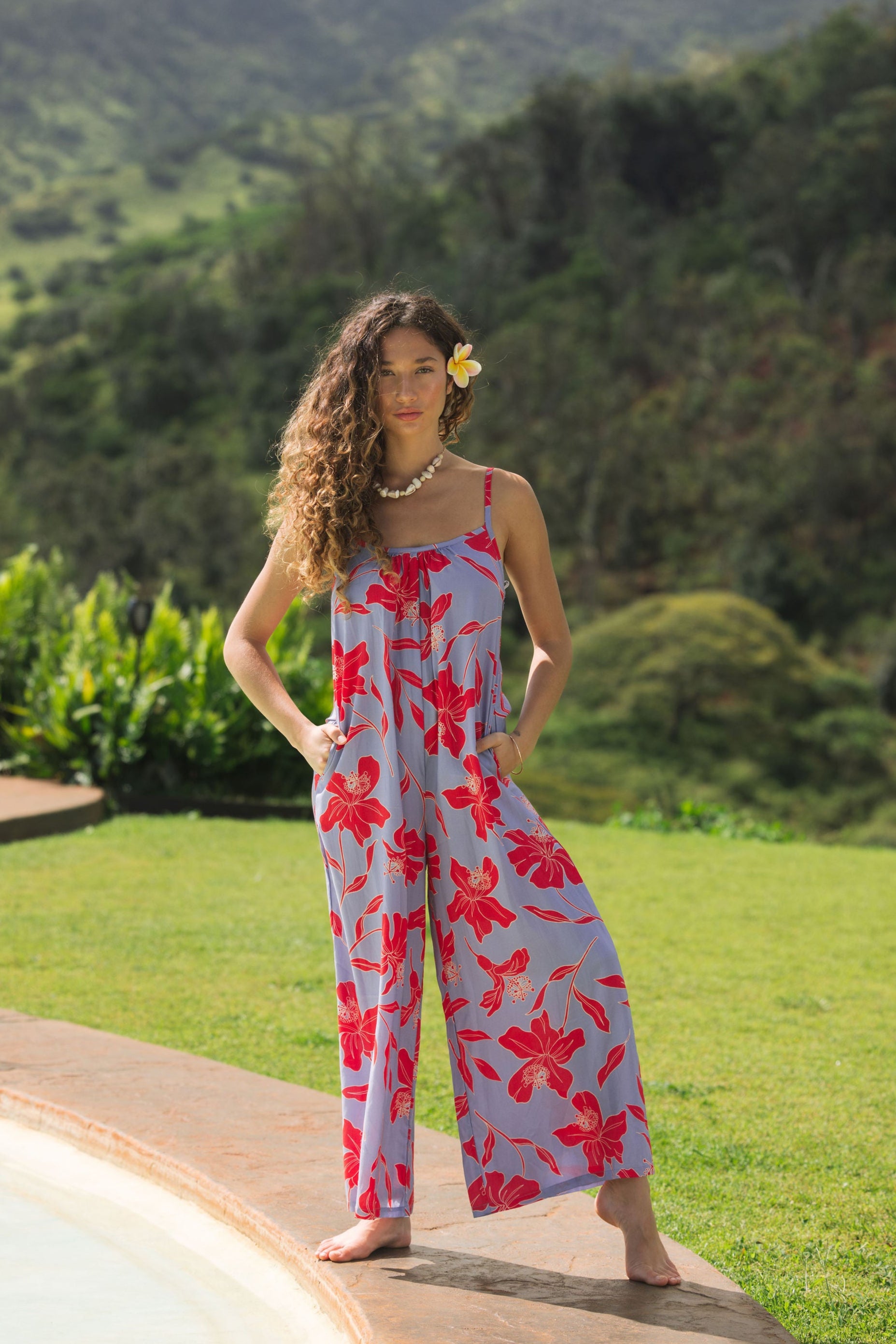 woman with brown hair wearing a jumpsuit with periwinkle background and bright red hibiscus print.