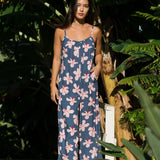 woman with black hair wearing a jumpsuit in a navy color with pink hibiscus blossoms