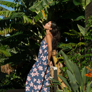 woman with black hair wearing a jumpsuit in a navy color with pink hibiscus blossoms