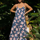 woman with black hair wearing a jumpsuit in a navy color with pink hibiscus blossoms
