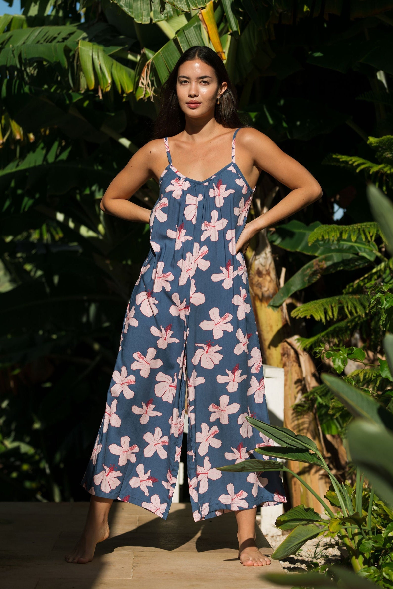 woman with black hair wearing a jumpsuit in a navy color with pink hibiscus blossoms