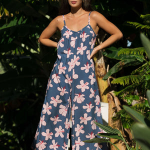 woman with black hair wearing a jumpsuit in a navy color with pink hibiscus blossoms
