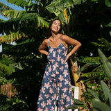 woman with black hair wearing a jumpsuit in a navy color with pink hibiscus blossoms