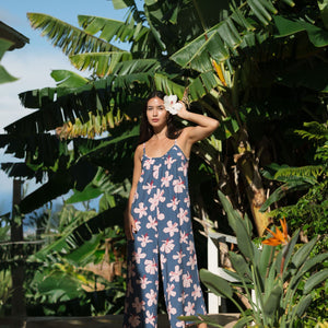 woman with black hair wearing a jumpsuit in a navy color with pink hibiscus blossoms