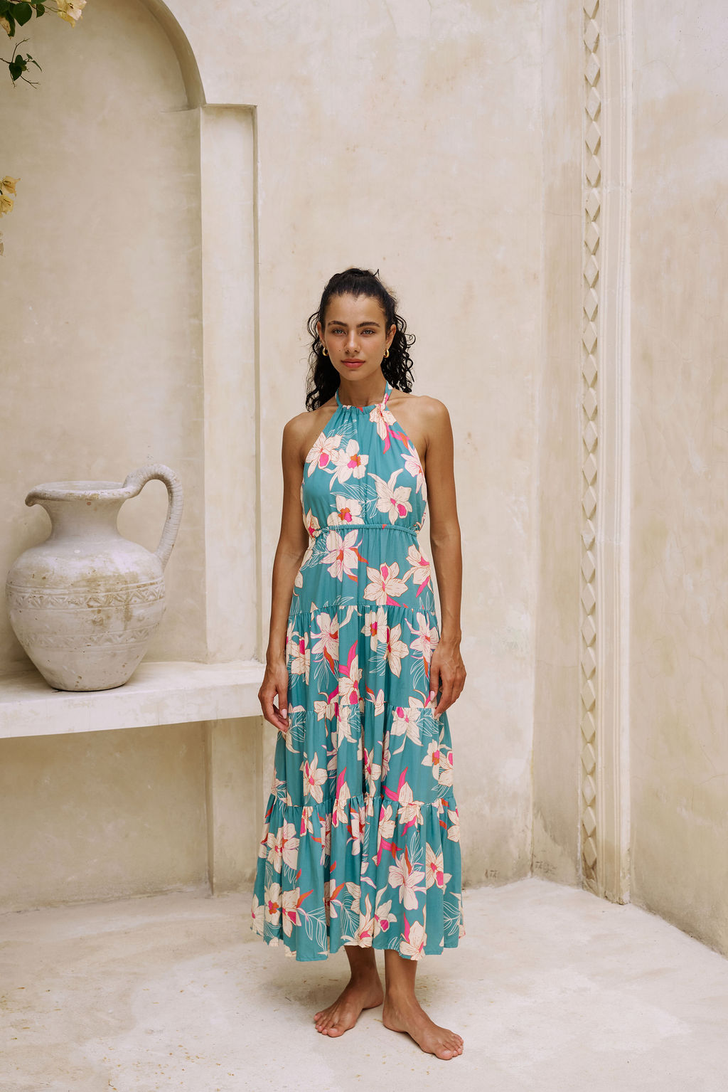 woman with brown hair wearing tiered halter maxi dress in teal with large cream colored orchids.