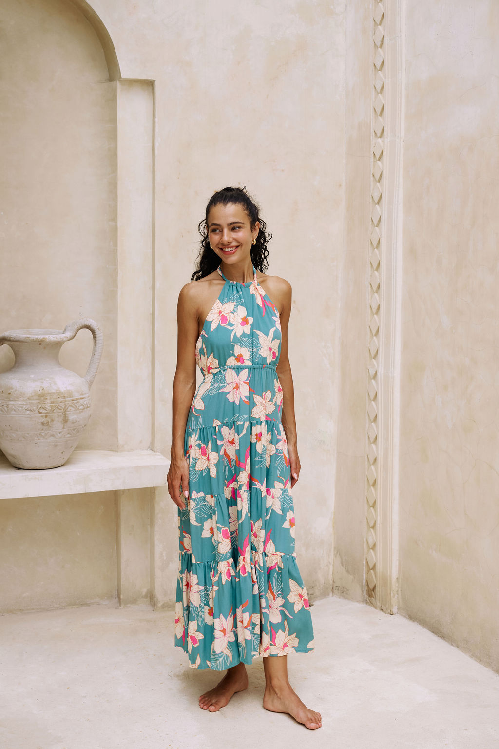 woman with brown hair wearing tiered halter maxi dress in teal with large cream colored orchids.
