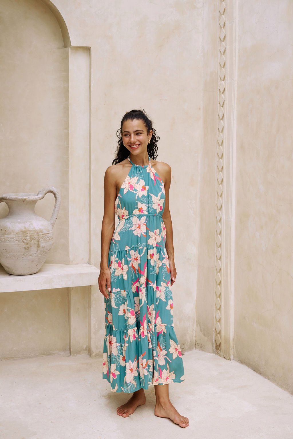 woman with brown hair wearing tiered halter maxi dress in teal with large cream colored orchids.